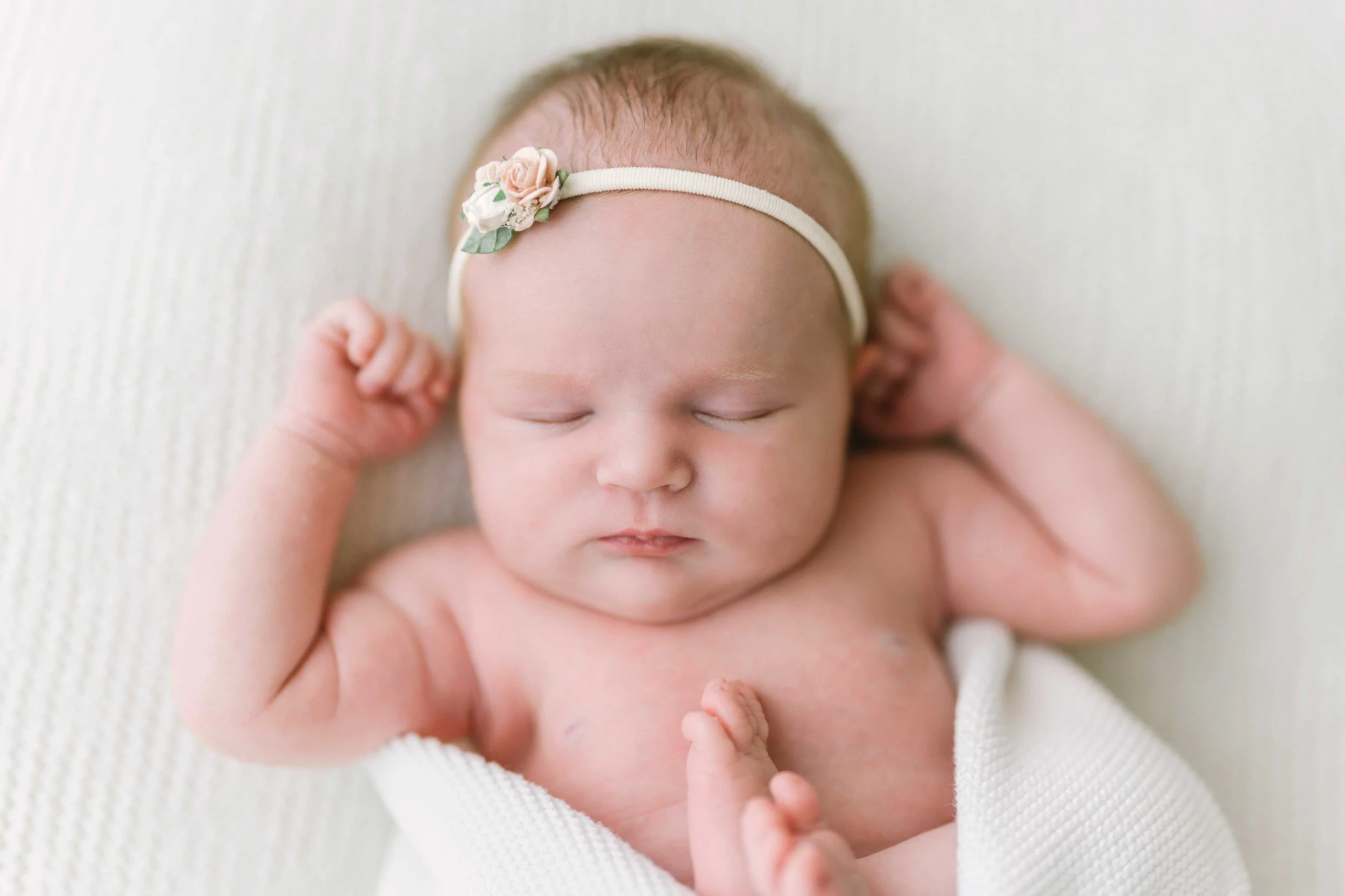 Wrapped newborn baby sleeping on her side with tiny feet peeking out during photography session