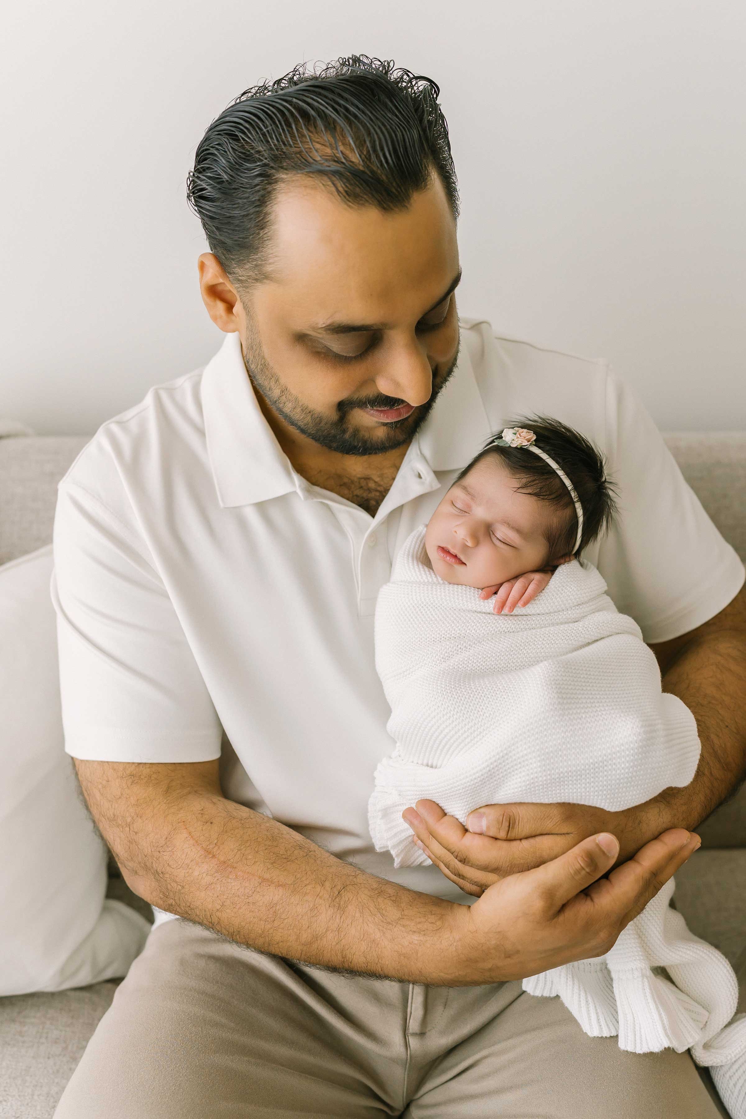 Dad holding a sleeping newborn baby girl in a white swaddle at our Grimsby studio
