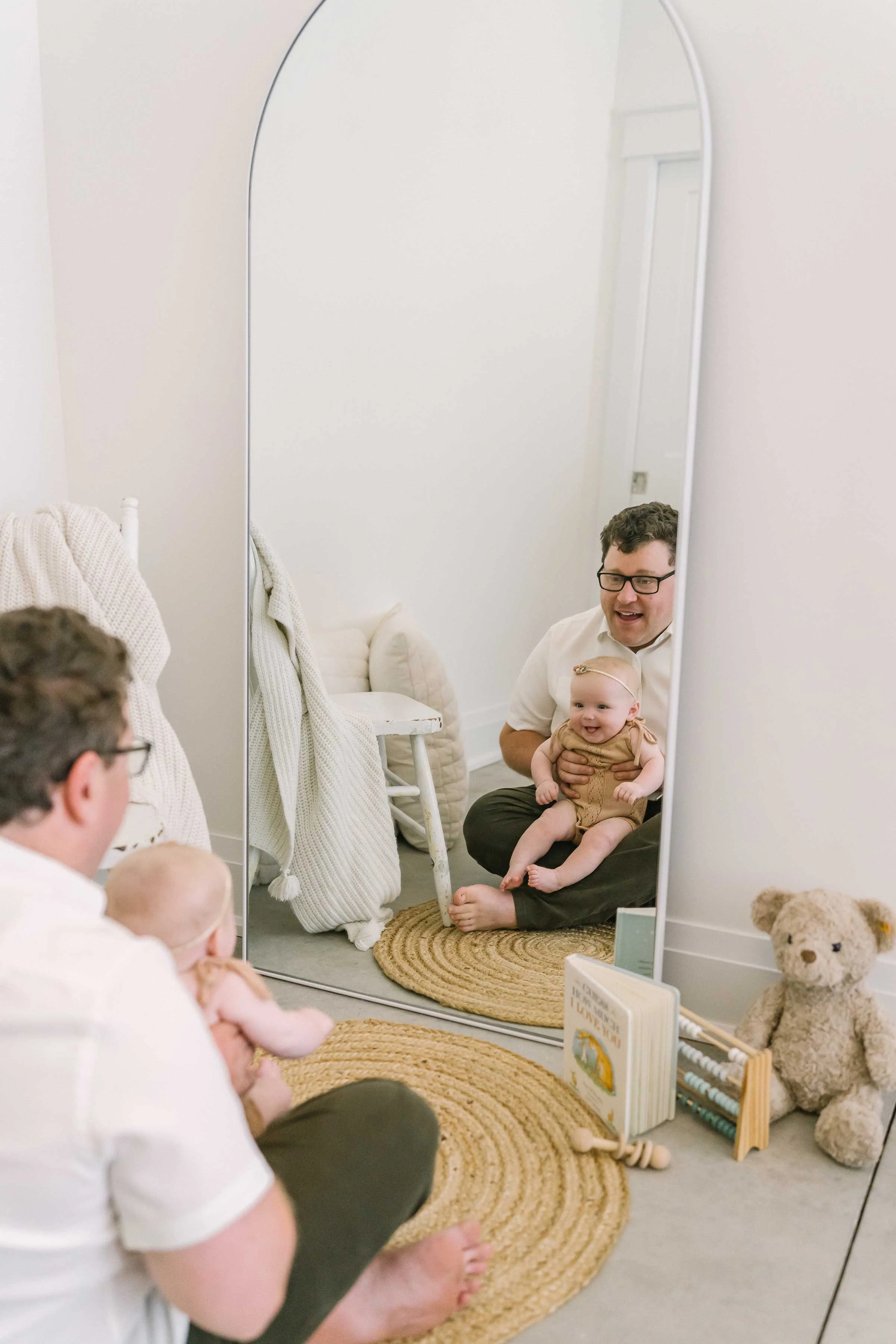 Dad and his 6 month old baby smiling at their reflection in a mirror in our Grimsby studio