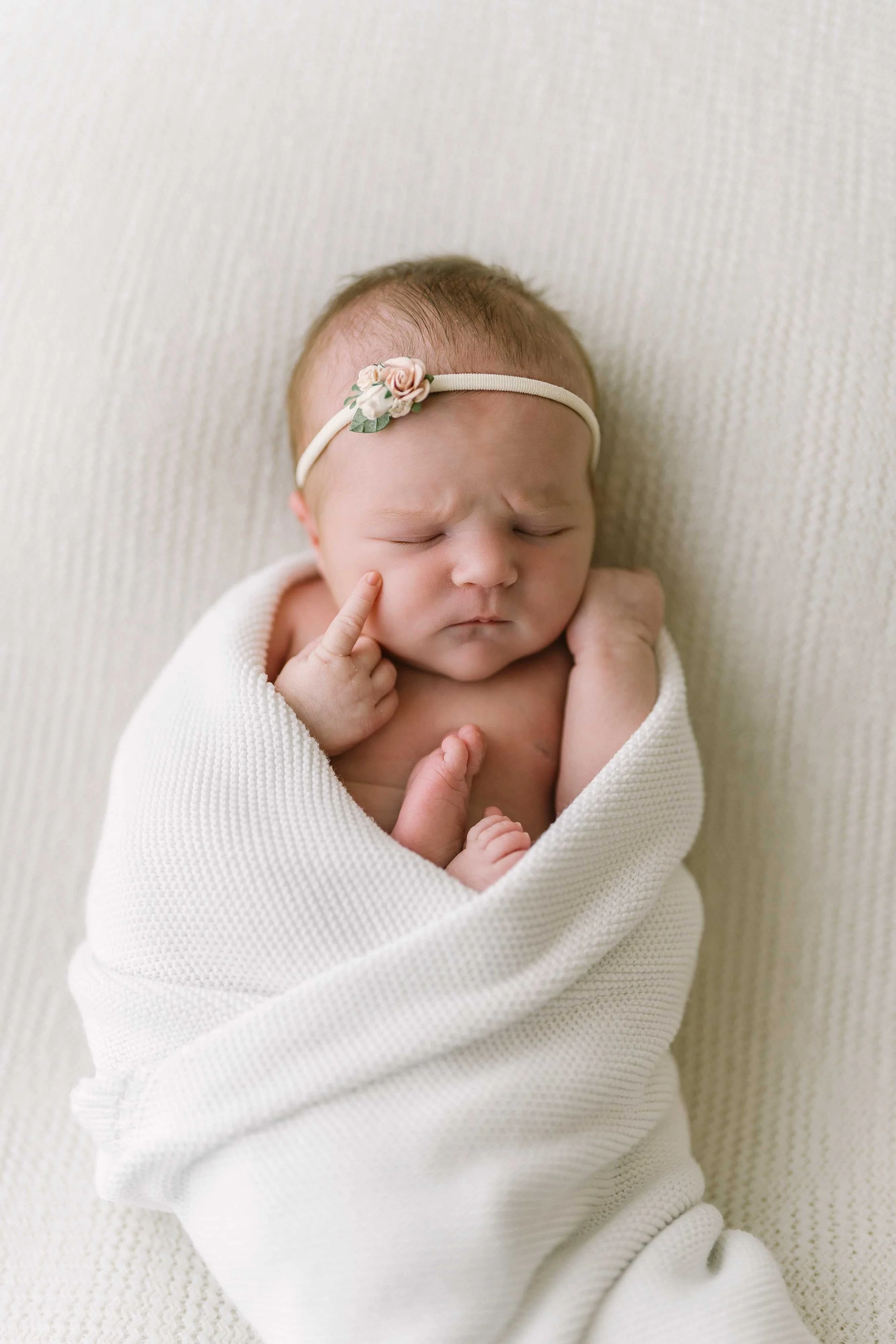Macro photo of newborn baby's tiny hand resting against her cheek during newborn session