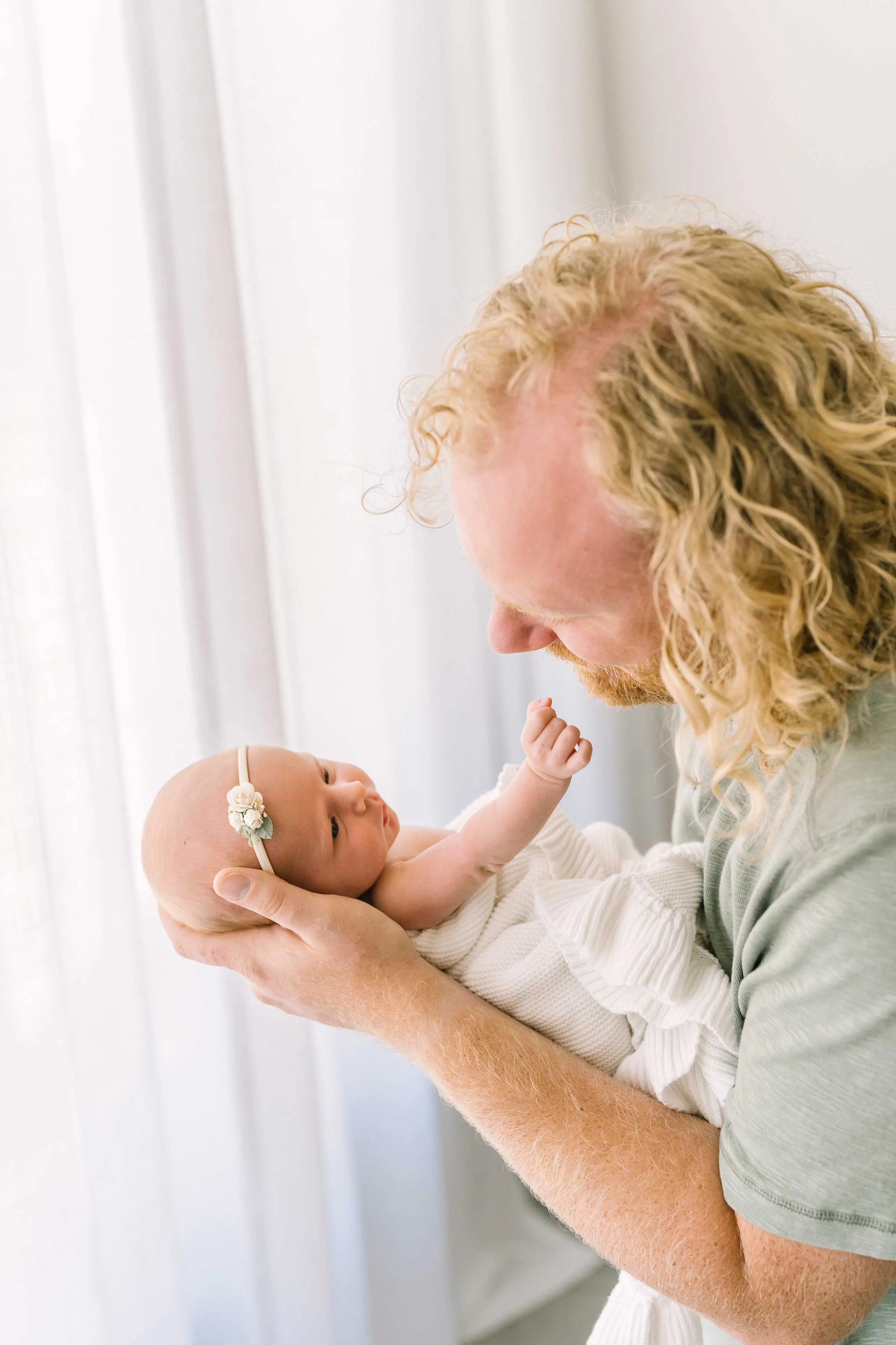 New dad with curly hair gazing at his newborn daughter by a studio window in Grimsby