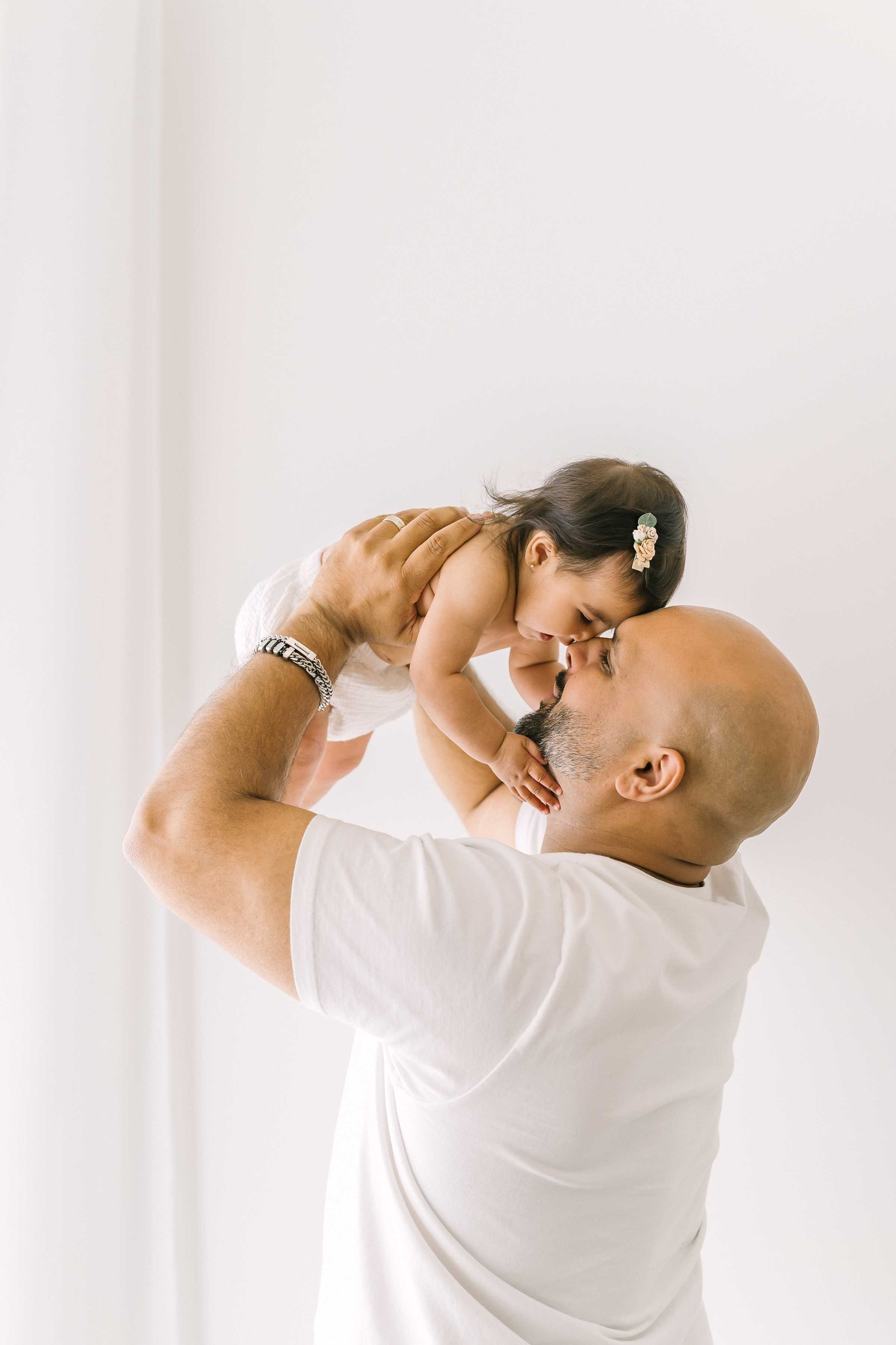 Dad lifting his baby girl up for a kiss on the forehead in a Grimsby studio