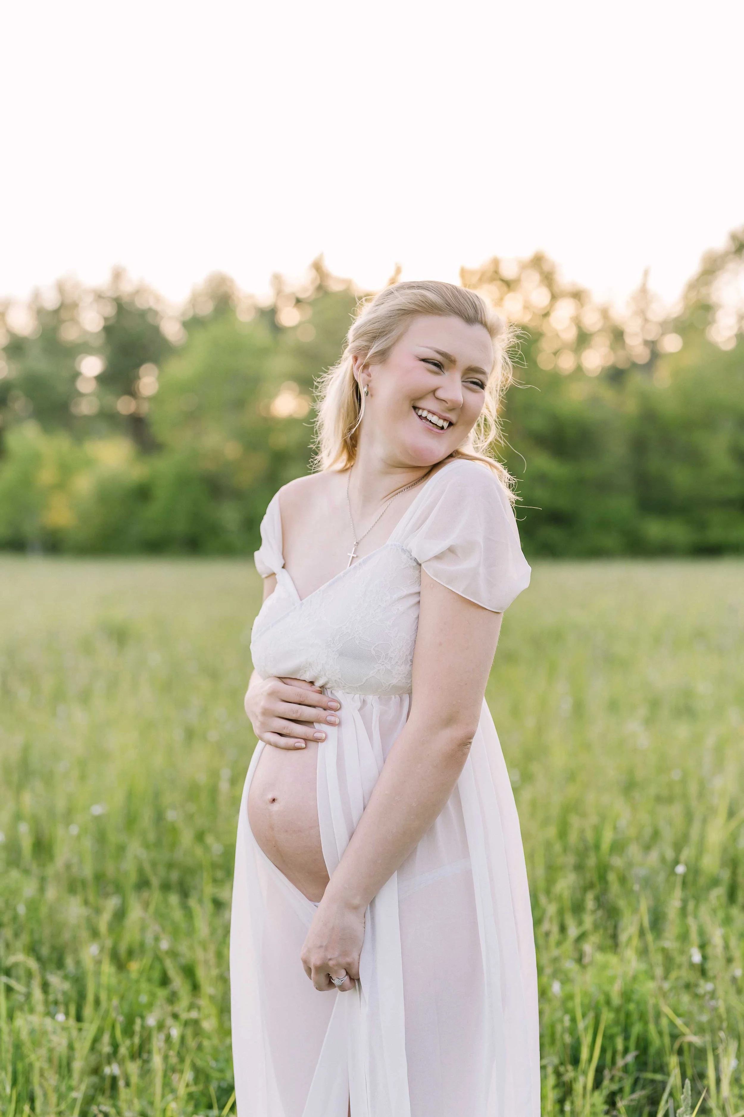 Pregnant woman standing among tall grass during sunset maternity photos