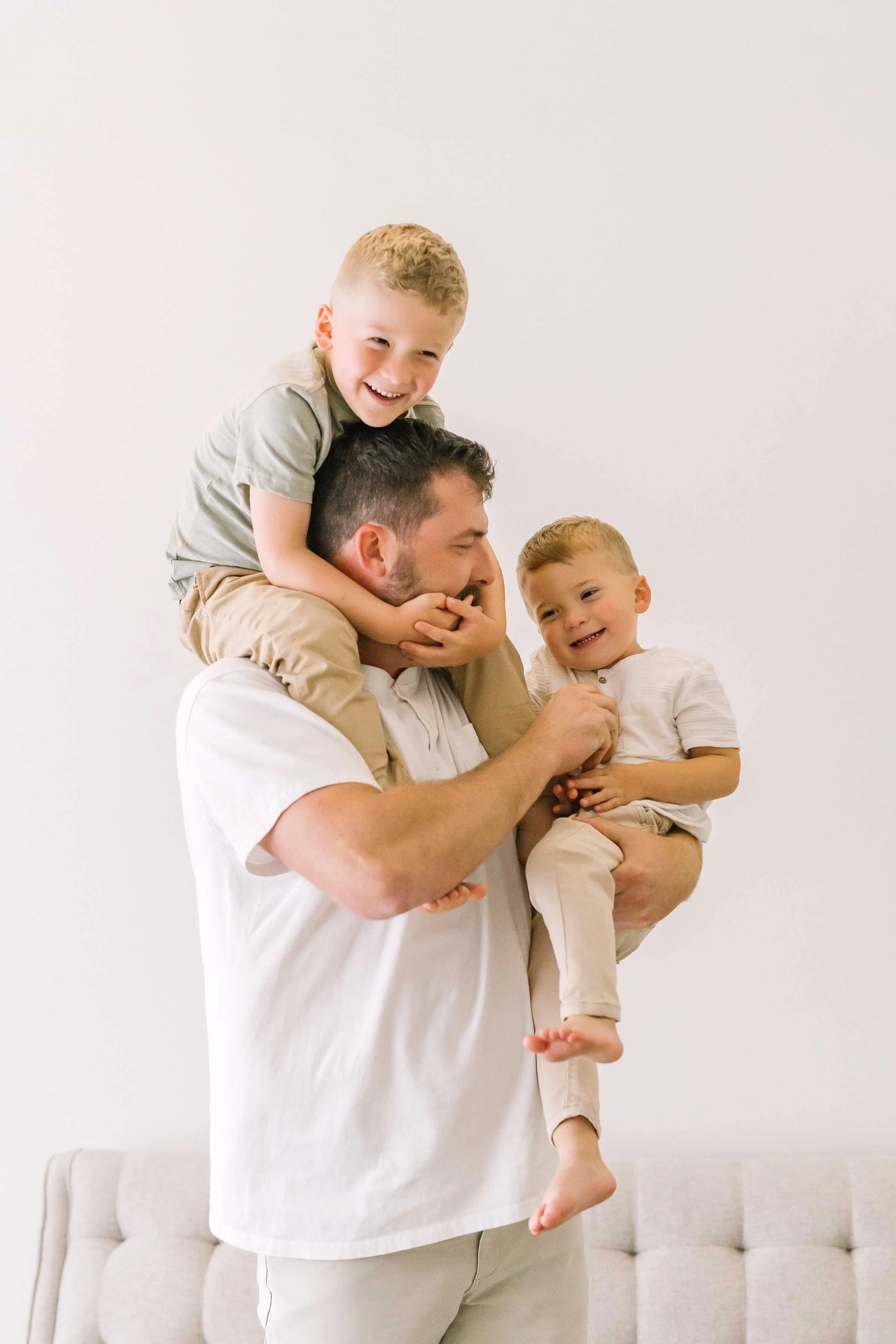 Dad carrying one son on his shoulders and holding another during a family session in Grimsby