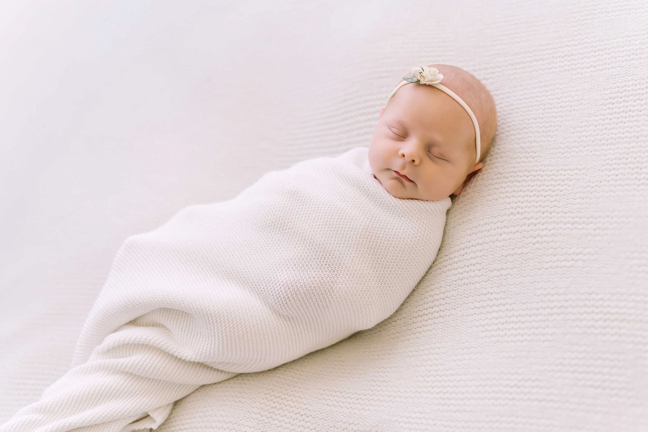 Lupia newborn baby wrapped in a white swaddle during a studio photography session