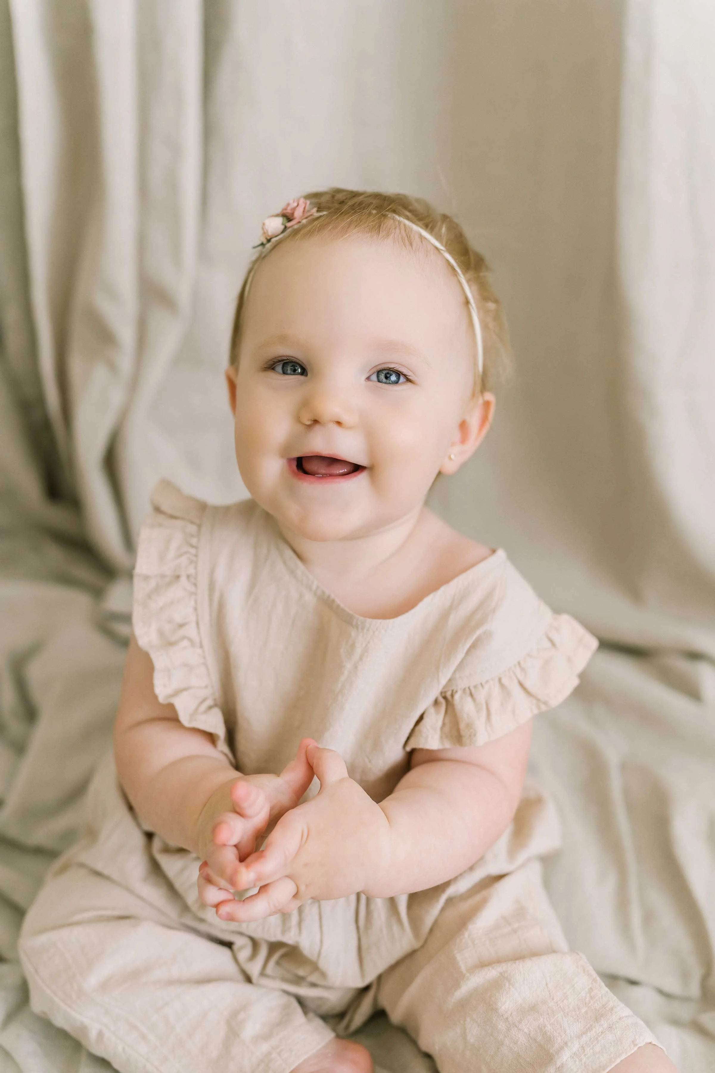 Smiling baby girl in a ruffled romper and headband during her Niagara baby milestone photos