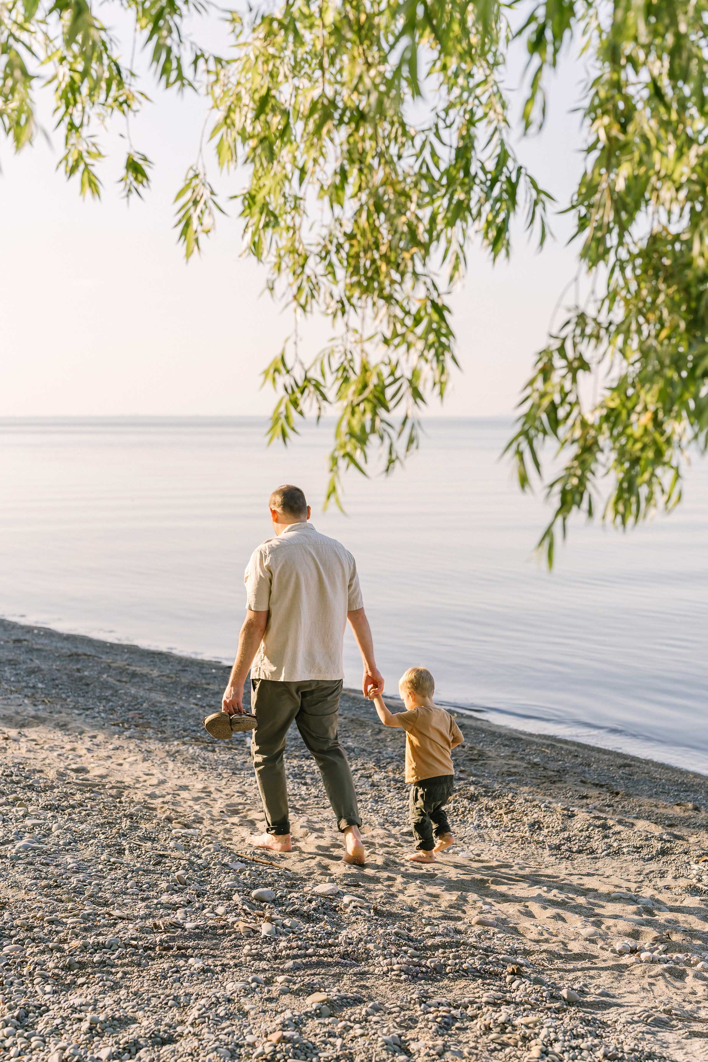 Dad walking hand in hand with his toddler on a Niagara beach at sunset
