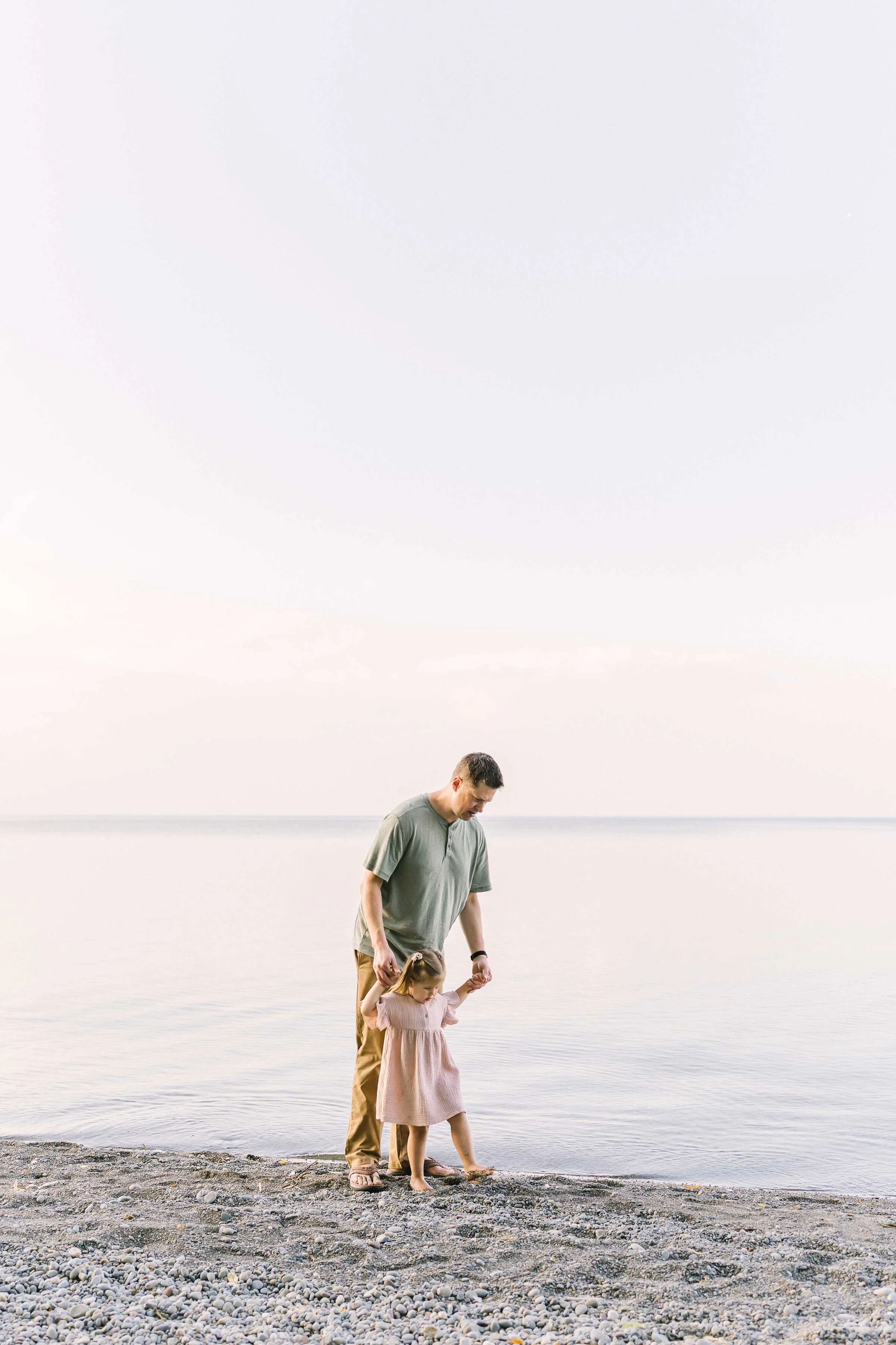 Dad holding his toddler daughter's hands at the Lake Ontario shoreline in Niagara