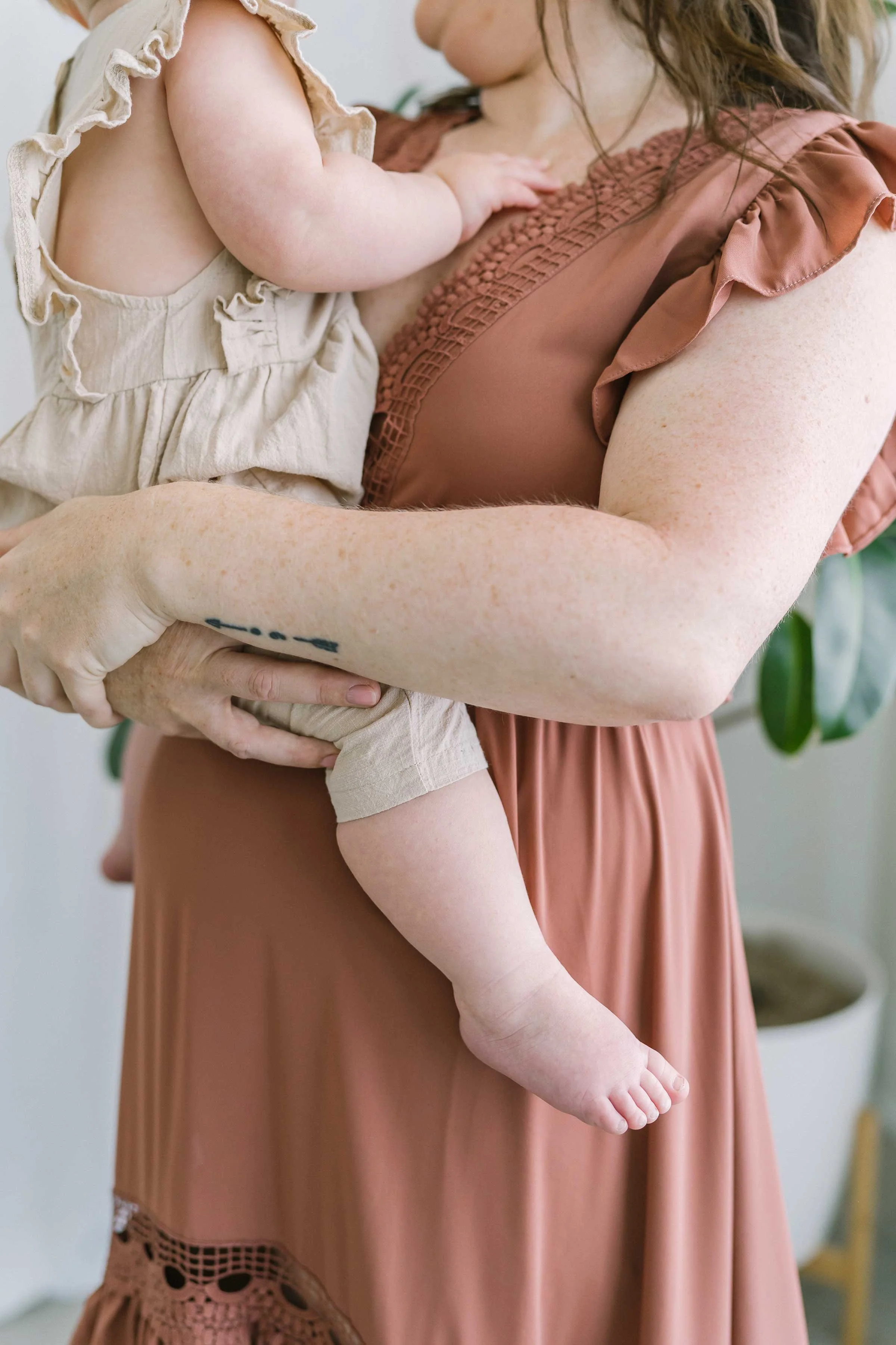 Baby girl's chubby arm and little legs as mom holds her close in our Grimsby studio