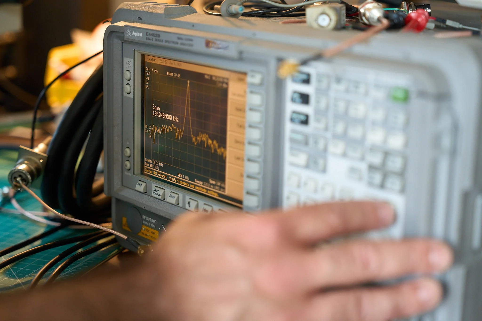 An oscilloscope displaying a frequency spectrum and a person's hand pressing buttons on the device.