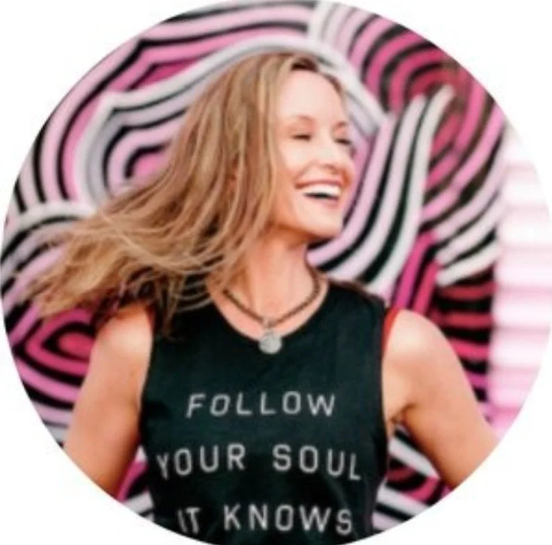 Woman smiling with flowing hair, wearing a black shirt with inspirational text "FOLLOW YOUR SOUL IT KNOWS," against a colorful abstract geometric background.