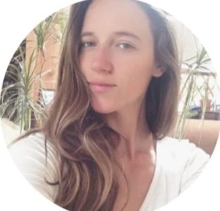 Woman with long hair smiling indoors with plants in the background