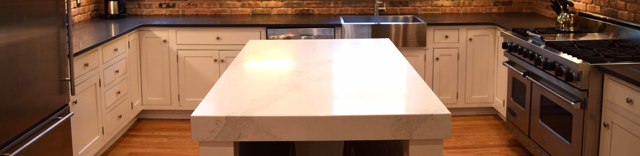 Engineered quartz countertops featured on the island above in a white marble pattern and on the surrounding countertops in black.