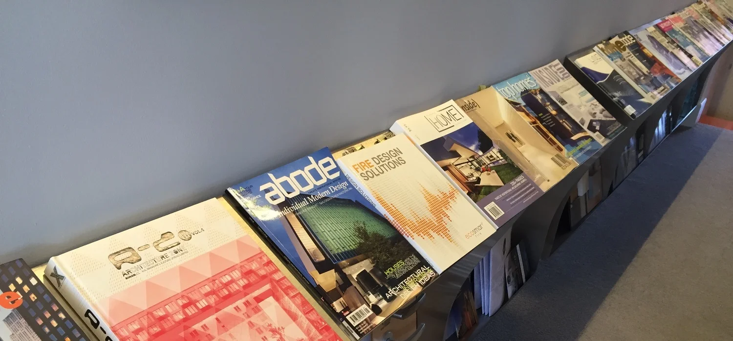 A long display of magazines on a black table against a gray wall, with various architecture and design magazines visible.