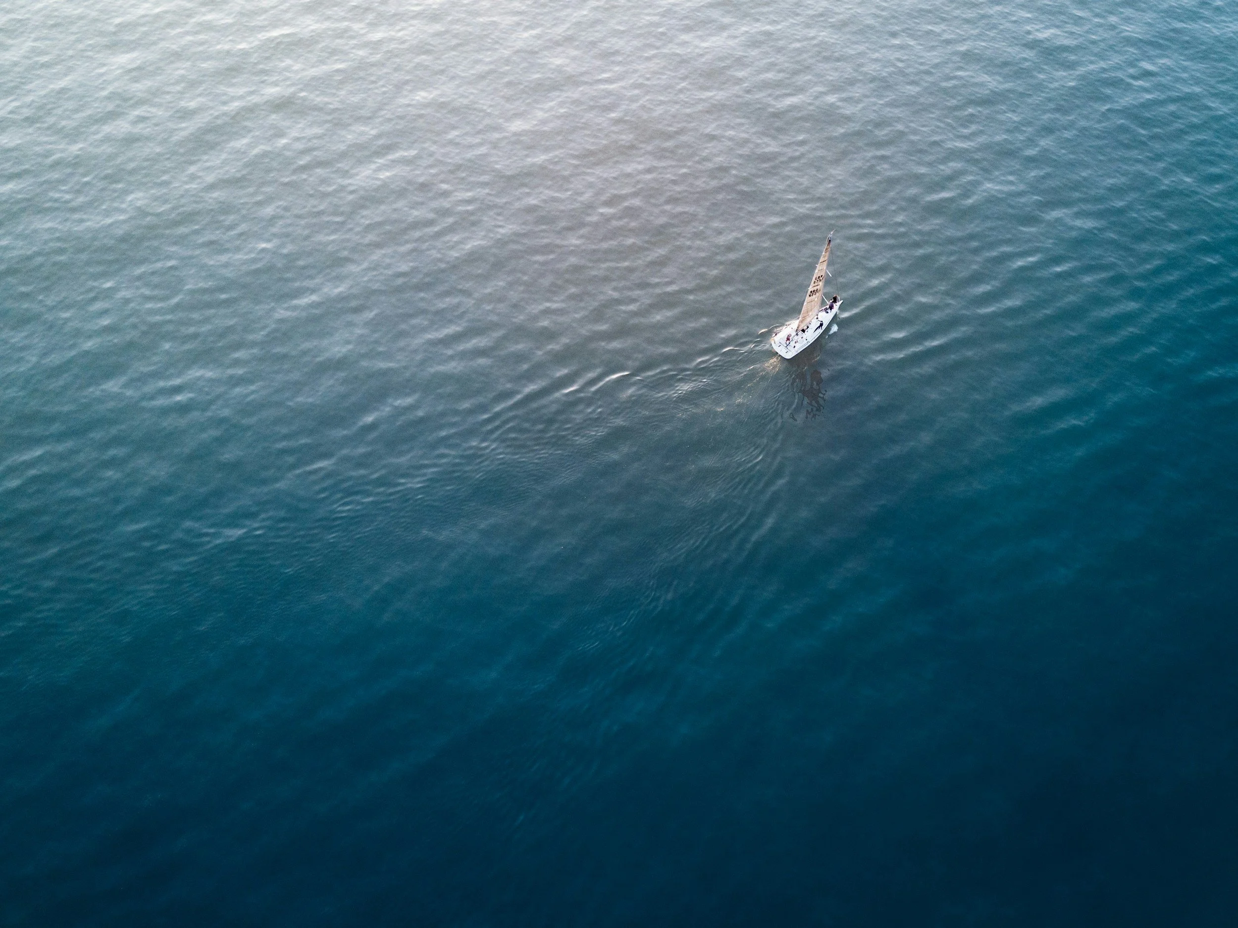 An aerial view of a small sailboat on the ocean with a couple of people on board.