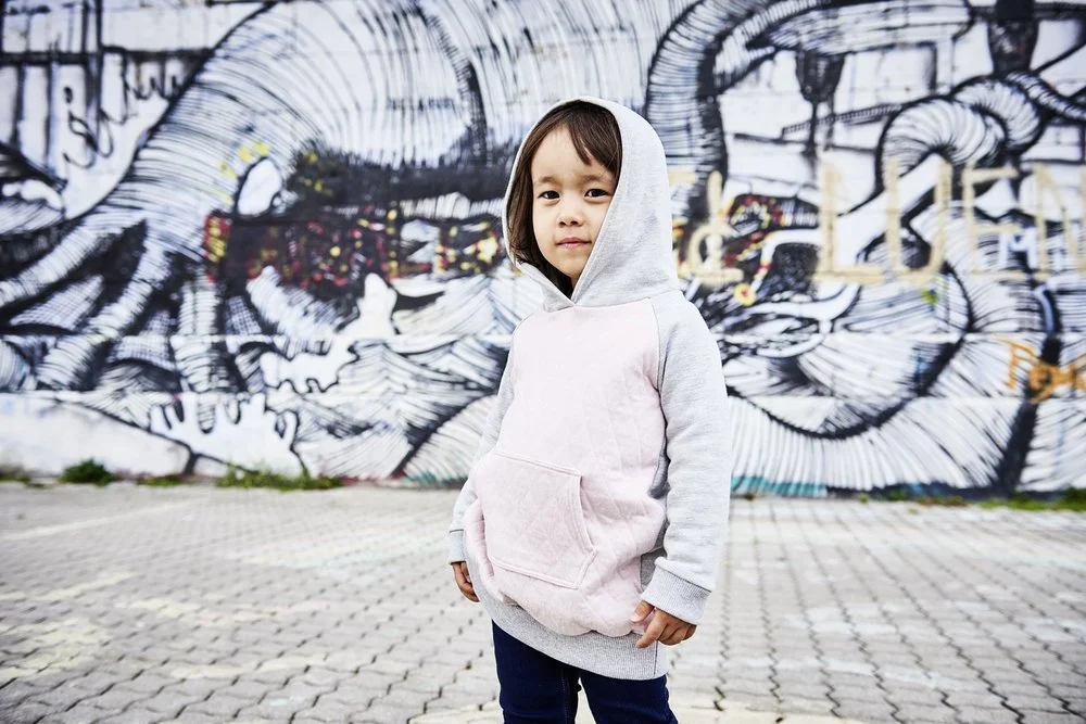 Mädchen in graurosa Kaputzenpulli steht am Donaukanal vor einem Graffiti und posiert für eine Modeaufnahme.