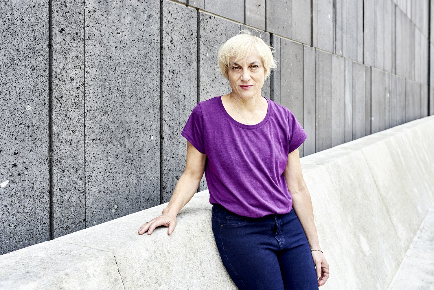 Portraitfoto Meg Stuart in lila Shirt an das Mumok gelehnt.