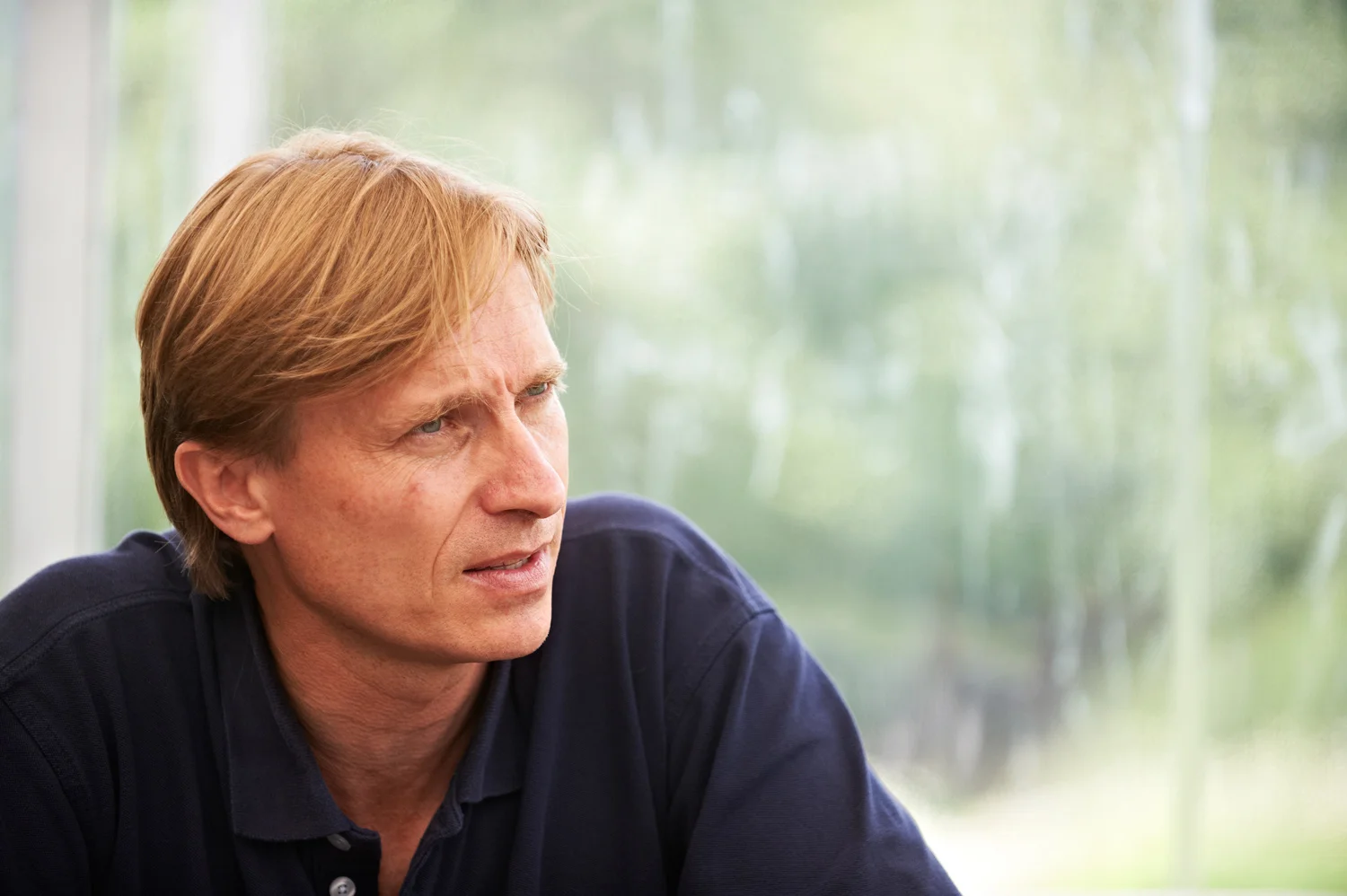 Mann mit blonden Haaren im Profil vor Glasscheibe