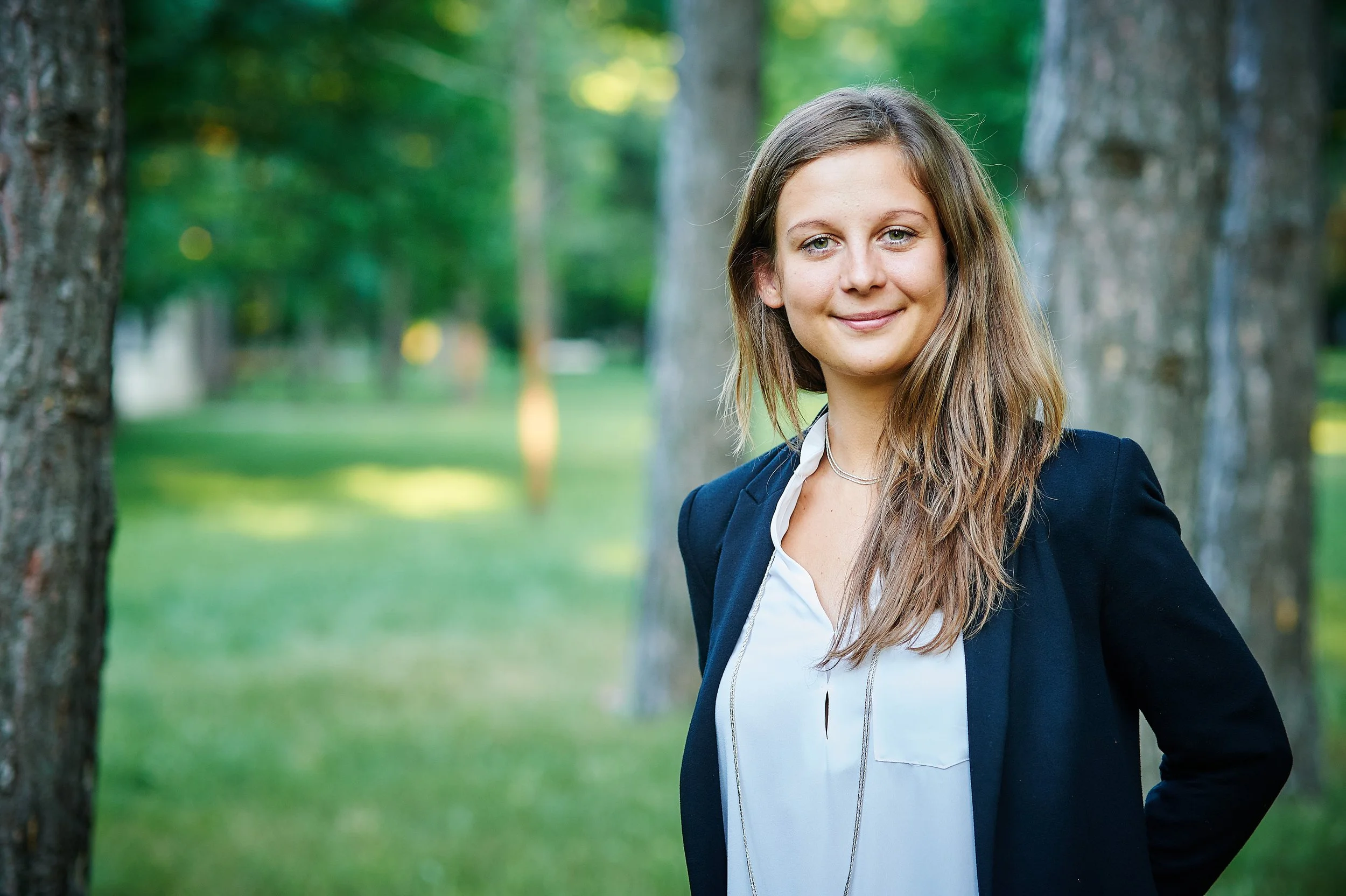 Frau im Businessoutfit steht im Park zwischen Bäumen