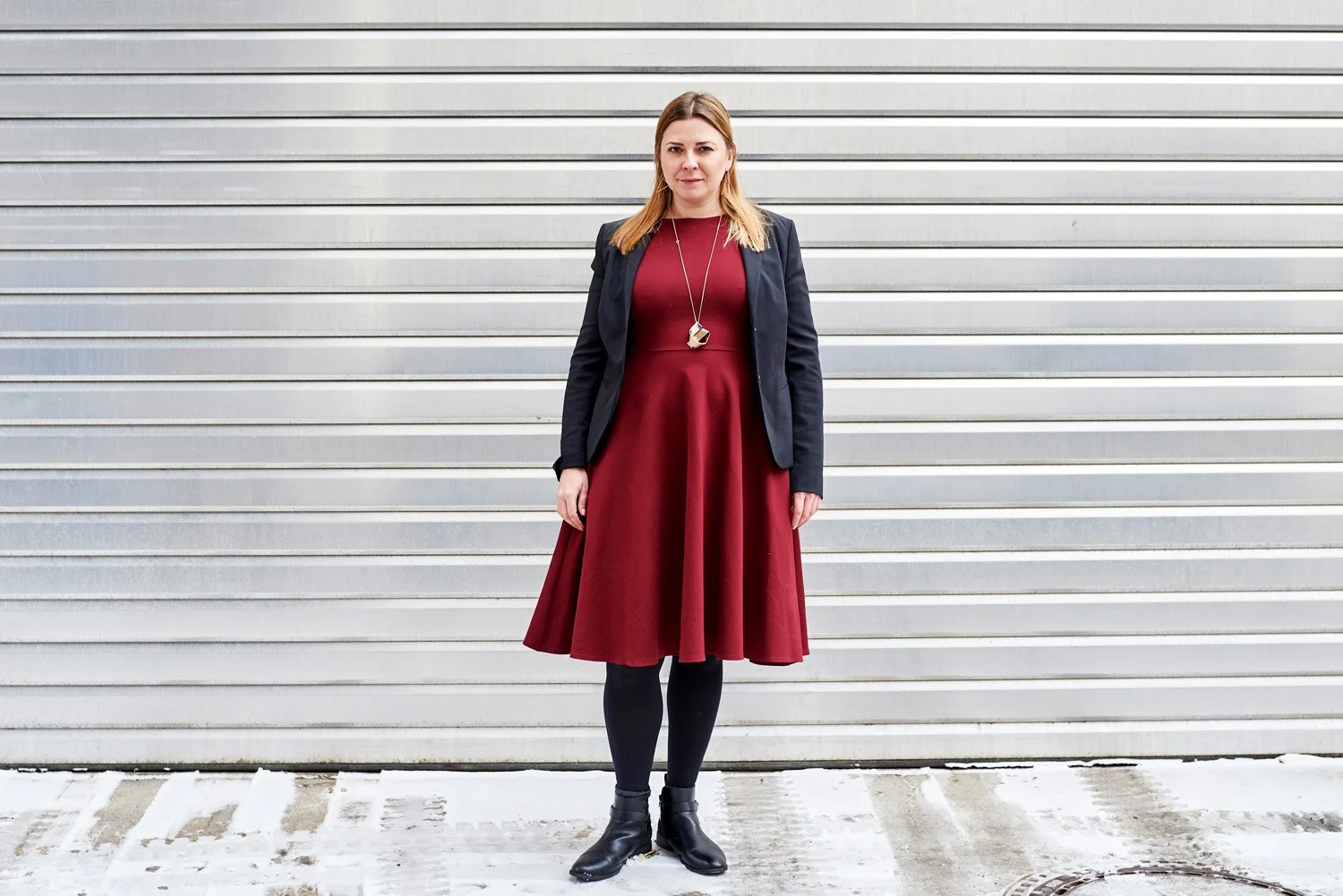 Frau mit rotem Kleid und schwarzem Blazer steht vor Garagentor