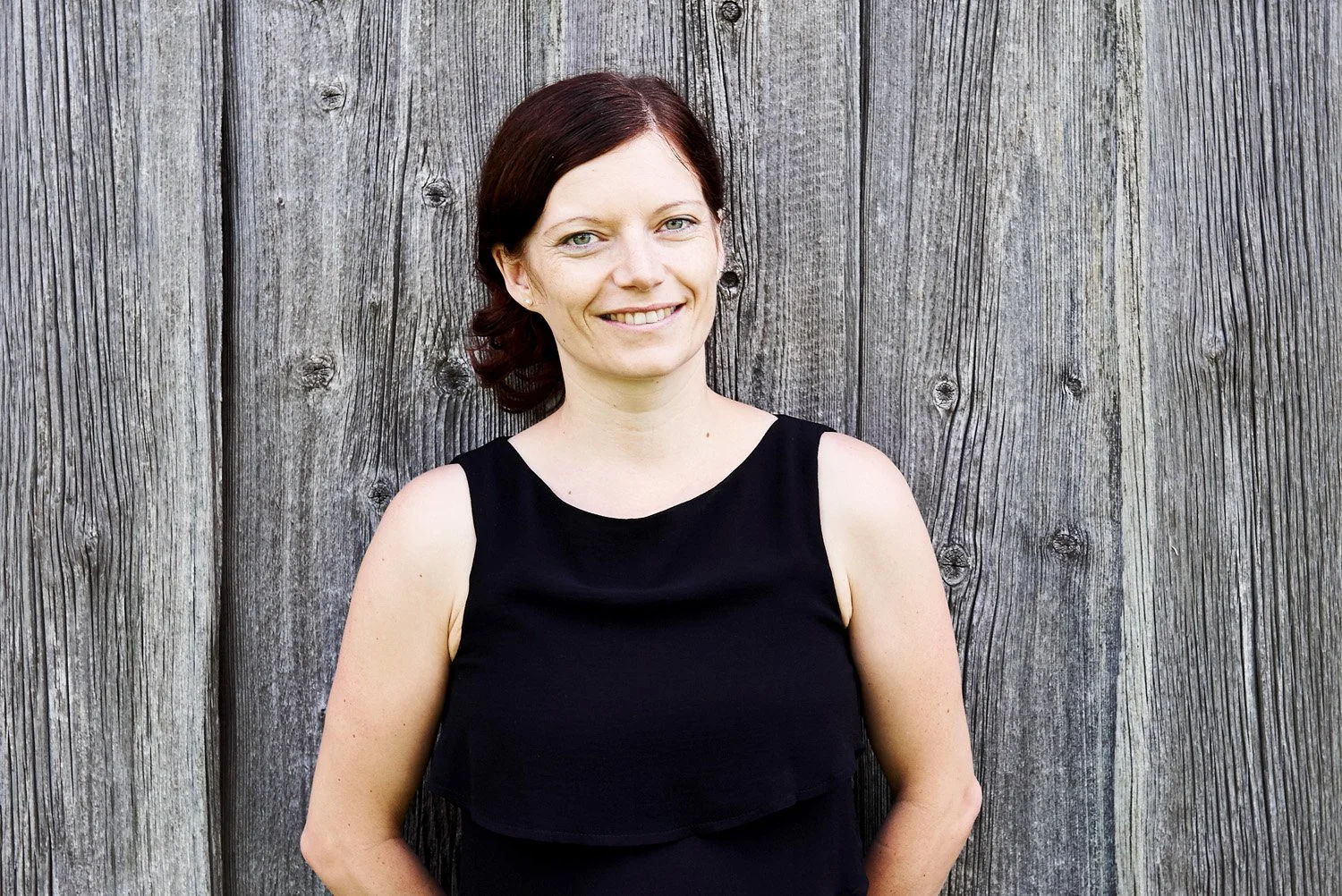 Portraitfoto einer Frau an eine graue Holzwand gelehnt