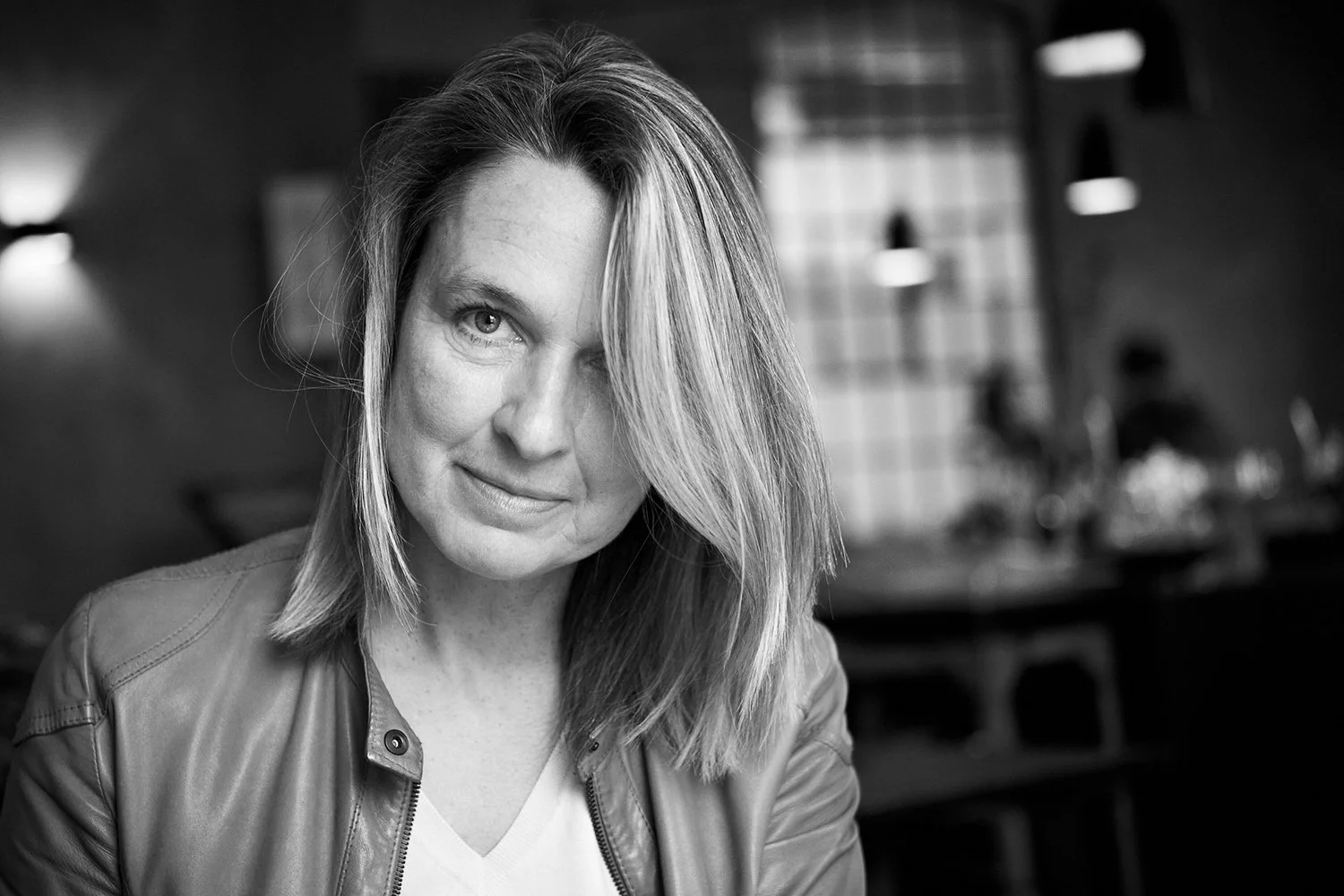 Schwarzweißfoto einer Frau mit offenem Haar und Lederjacke in einem Cafe