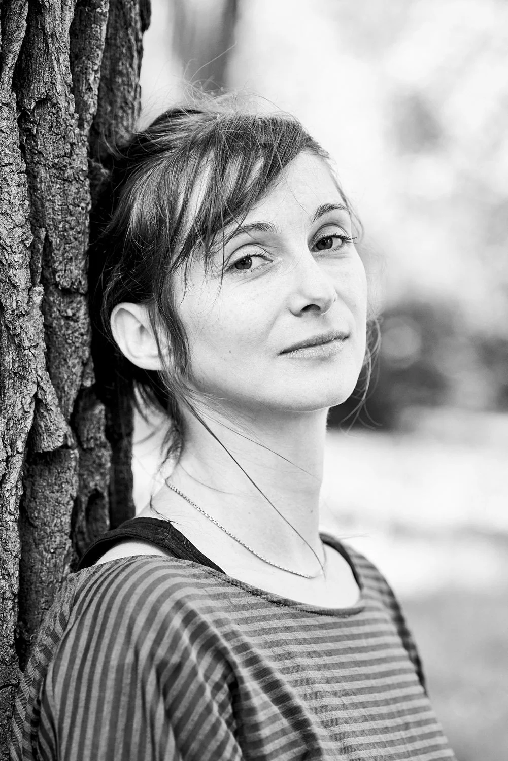 Portraitfoto einer Frau die im Park an einen Baum gelehnt steht