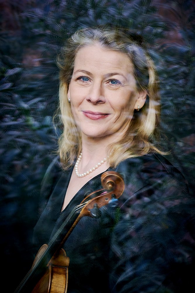 Foto einer Frau mit Geige und Perlenkette, durch ein Glas mit Lichtreflexionen fotografiert.