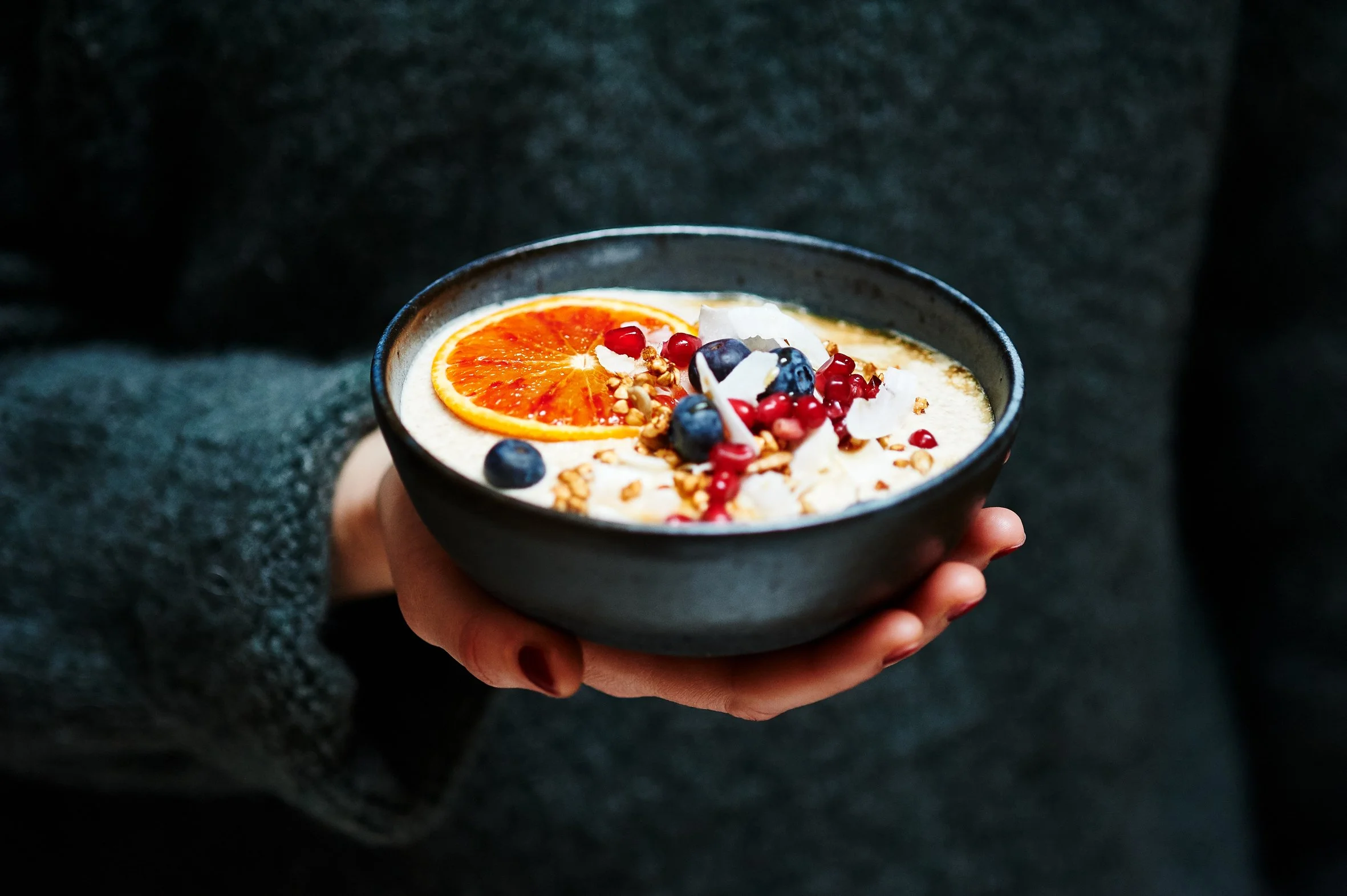Frau hält klene Schüssel in der Hand mit Porridge und Früchten darauf.