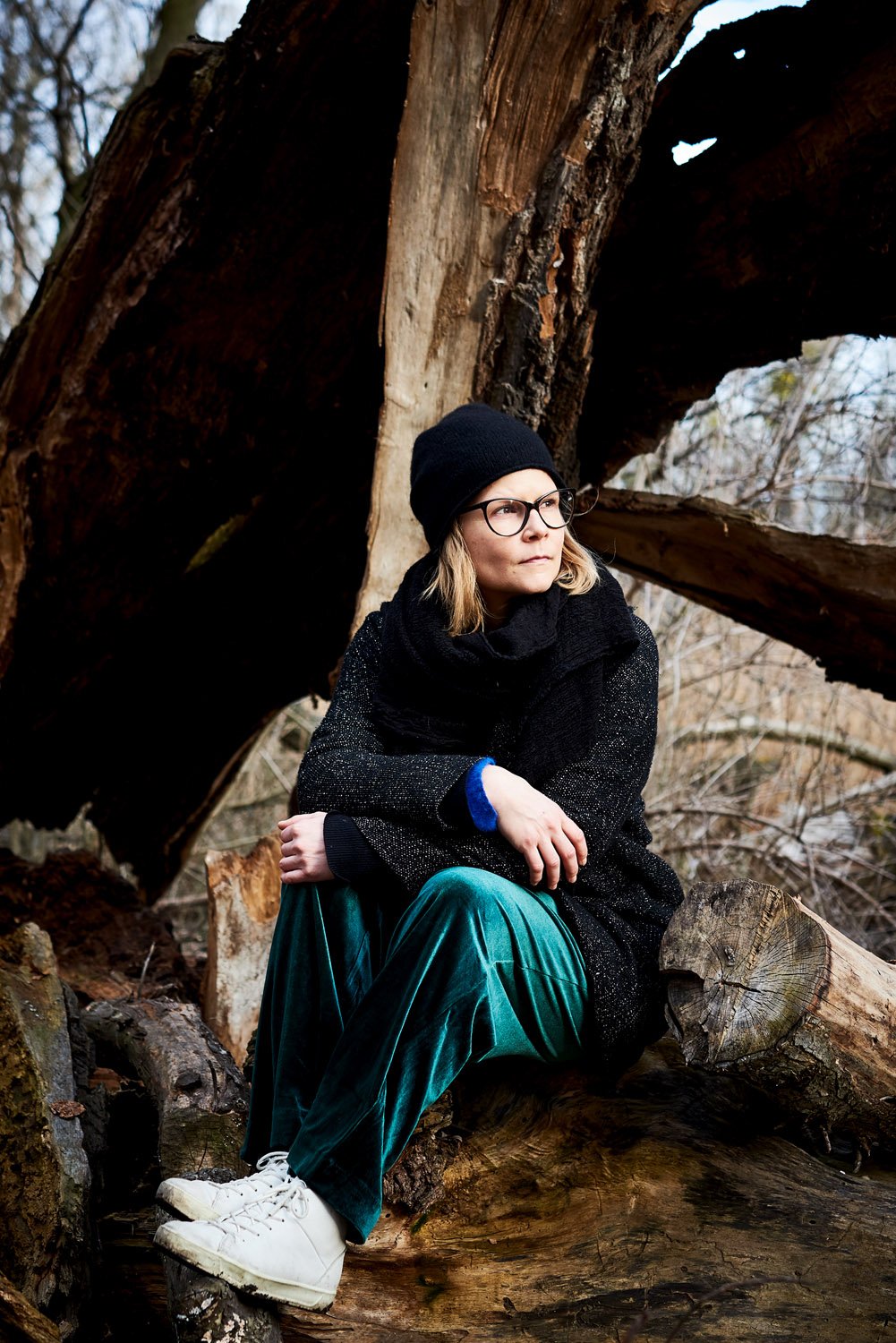 Foto einer jungen Frau mit schwarzer Wollhaube die auf einem Baumstamm sitzt