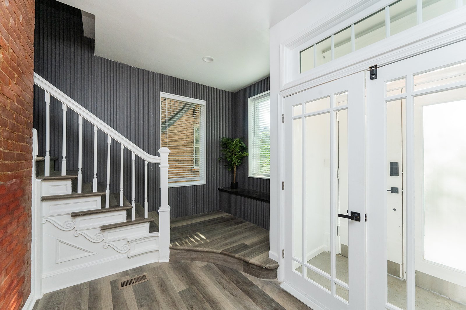 Interior of a modern entryway with white doors, a staircase with white railing, wood flooring, and a small plant.