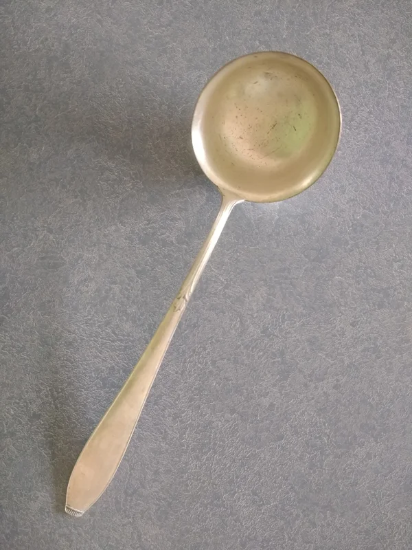 Silver plated ladle with worn plating and scratches in the bowl of the ladle.