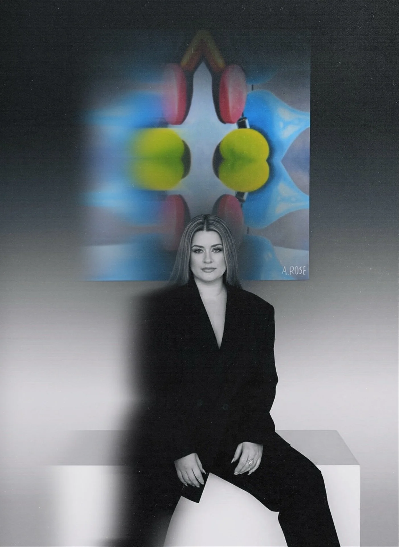 A woman with long hair dressed in a black suit sitting on a white cube in front of a colorful abstract painting of a face with large headphones.