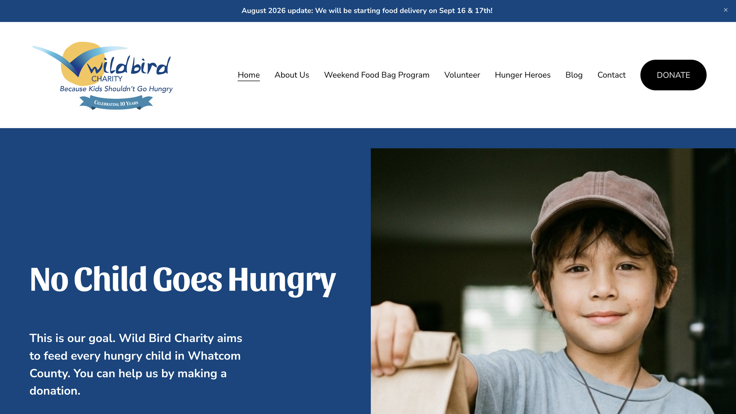 A boy wearing a gray shirt and a light pink cap smiling and holding a paper bag, part of a charity website with a blue header and a slogan about feeding hungry children.