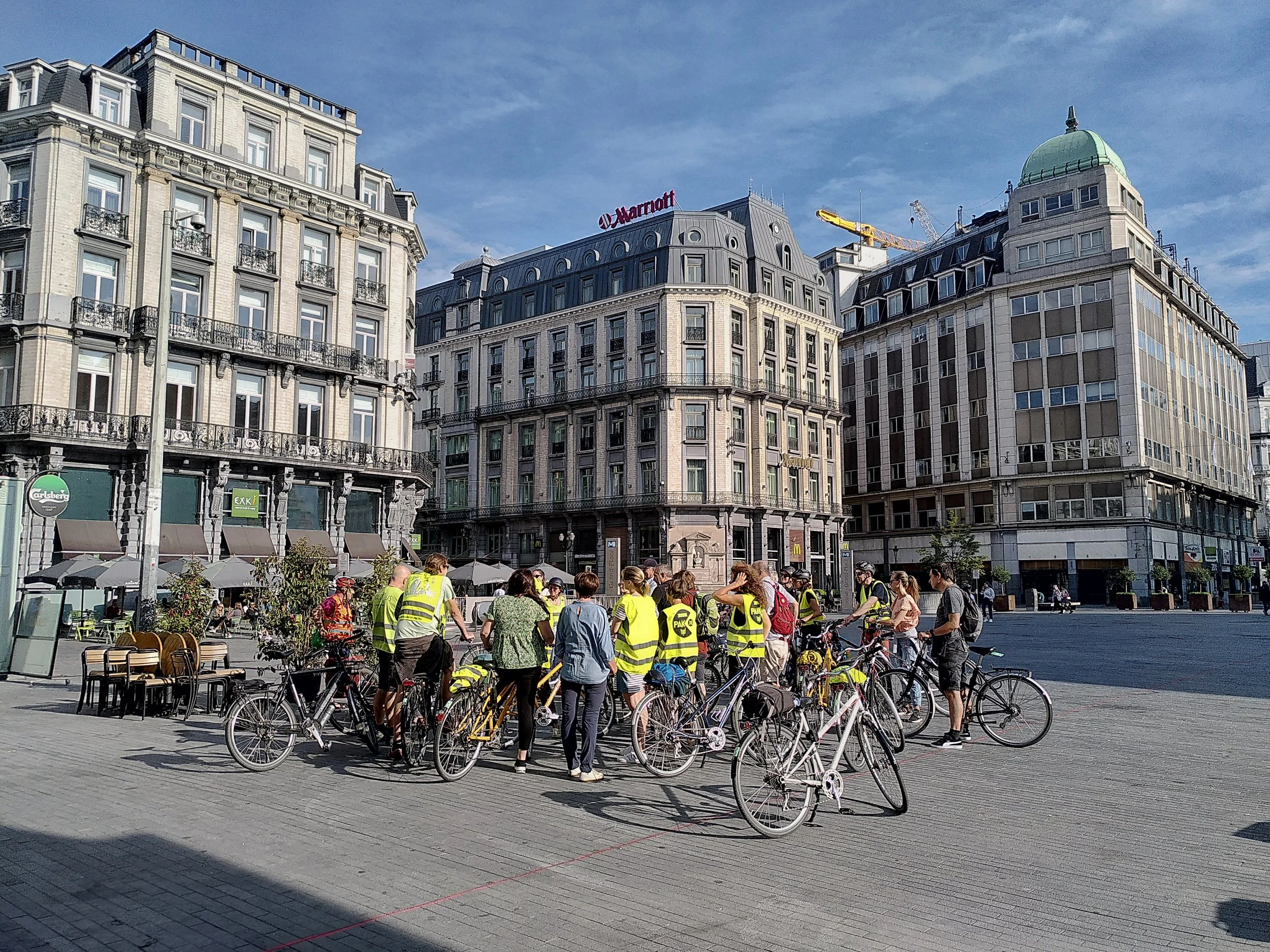 Groep fietsers op teambuilding op het Beursplein, omringd door historische gebouwen op een zonnige dag.