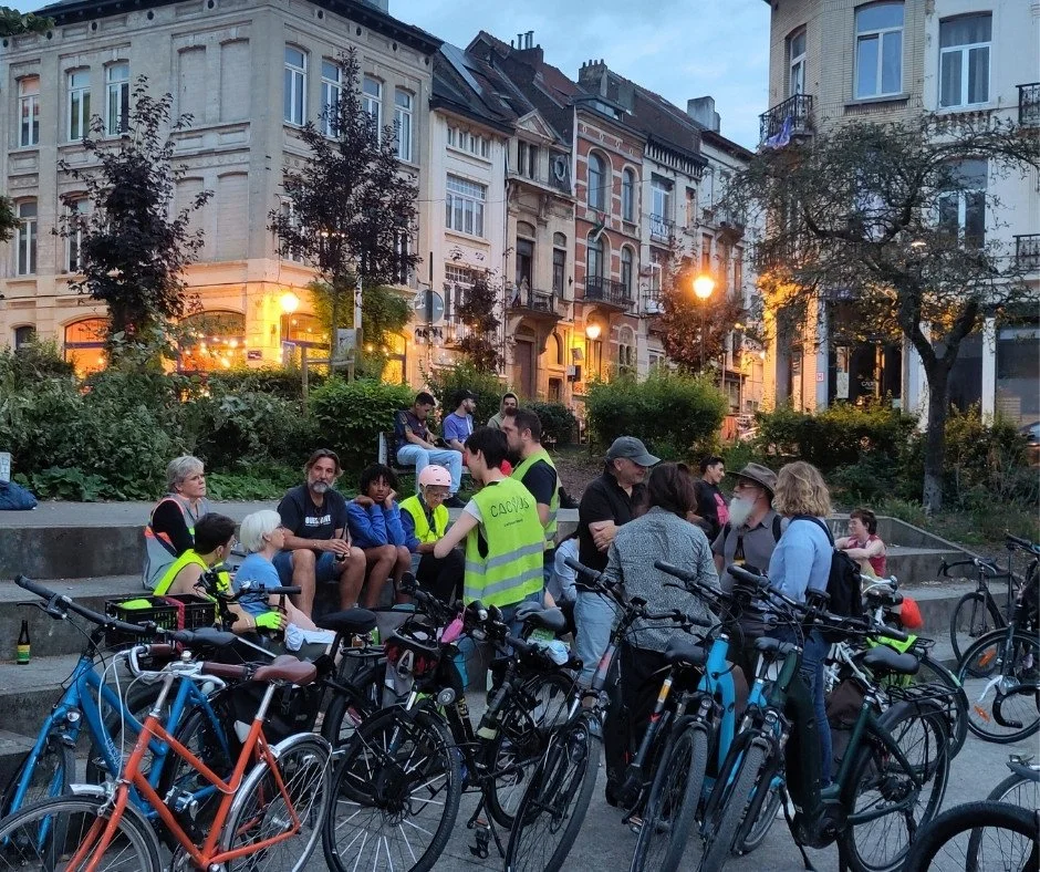 Een groep Brusselaars zitten op een plein in Sint-Gillis in Brussel. Ze doen mee aan een gegidste avondtour met de fiets die hen Brussel op een originele manier laat herontdekken.