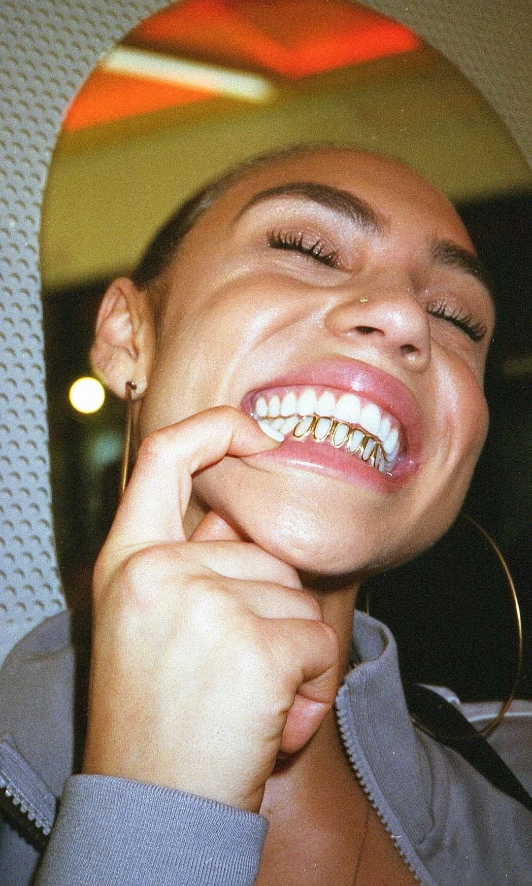 A woman with a bright smile showing gold grills on her teeth, enjoying a fun moment.