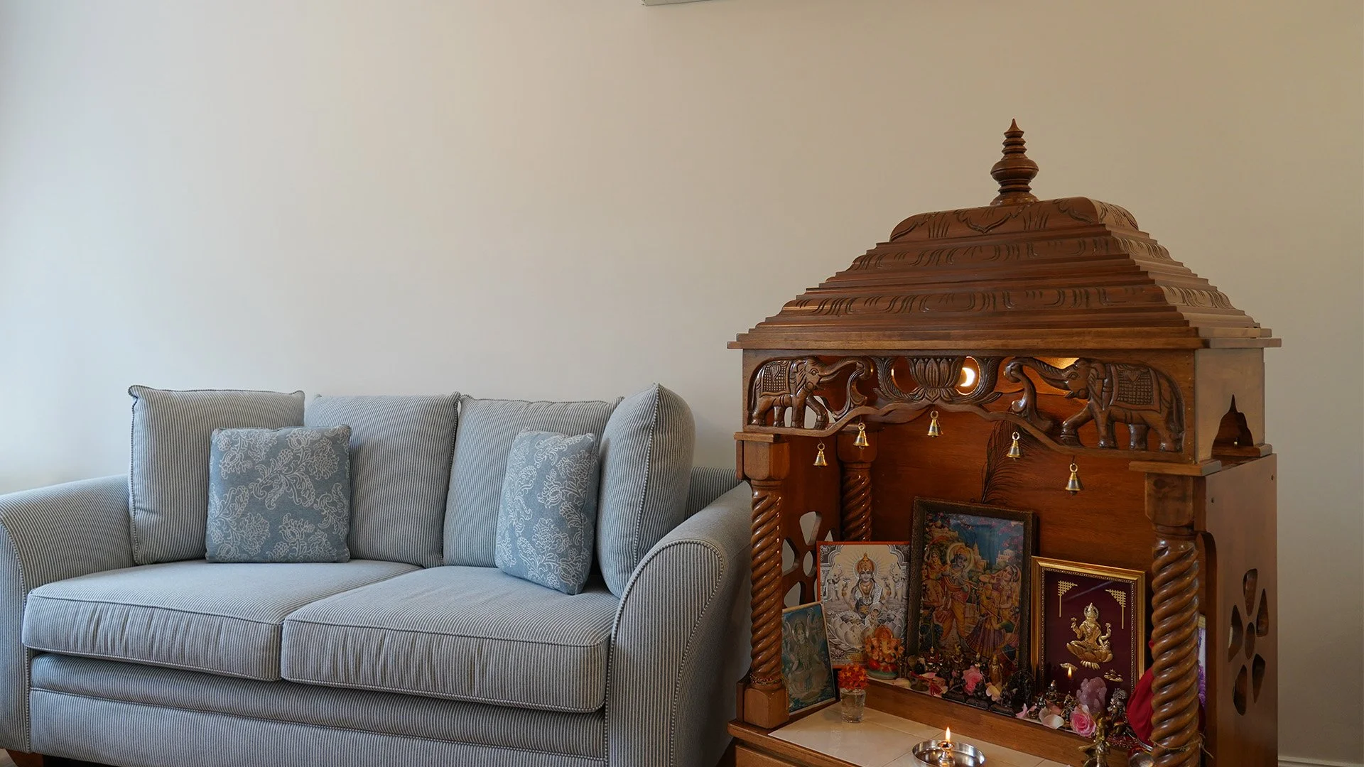 Traditional wooden home mandir placed in a living room, showcasing elegant Indian craftsmanship and a peaceful spiritual space for Hindu prayer.