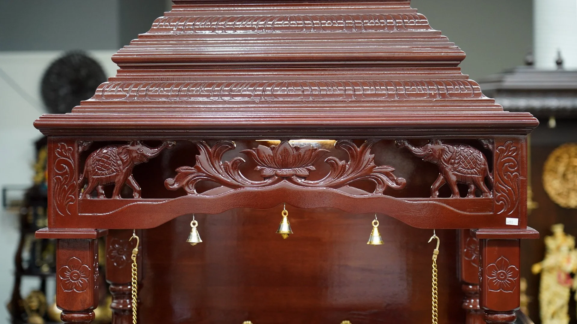 Close-up of detailed handcrafted wooden mandir carvings featuring traditional Indian floral patterns and hanging bells.