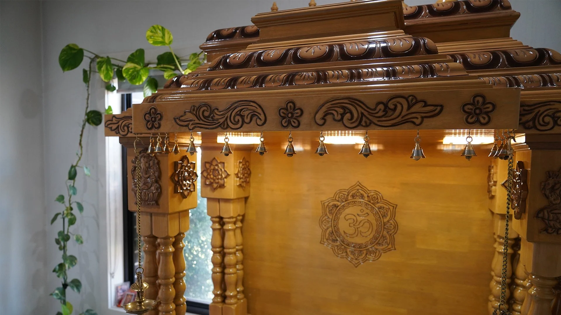Handcrafted wooden mandir with intricate traditional carvings and hanging bells, designed as a home temple for Hindu prayer and spiritual practice. Premium Indian mandir furniture suitable for modern homes.
