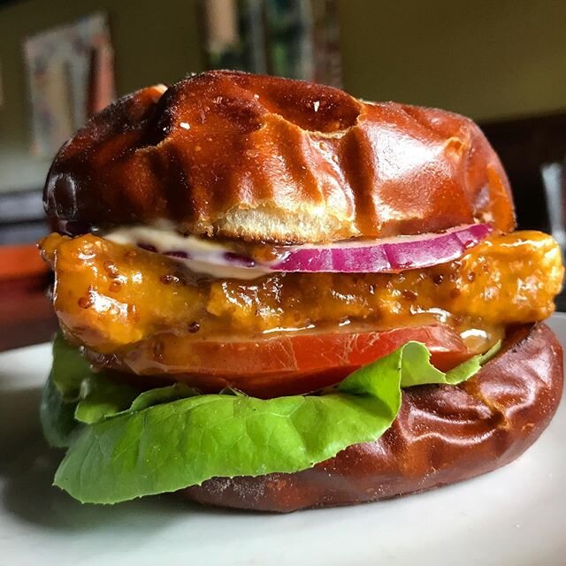 CORNMEAL-CRUSTED TEMPEH SANDWICH with miso-maple-mustard sauce, butter lettuce, tomato, red onion &amp; chile aioli on a pretzel bun - order online for curbside pickup Saturday and Sunday from 2pm-6pm (link in bio)!