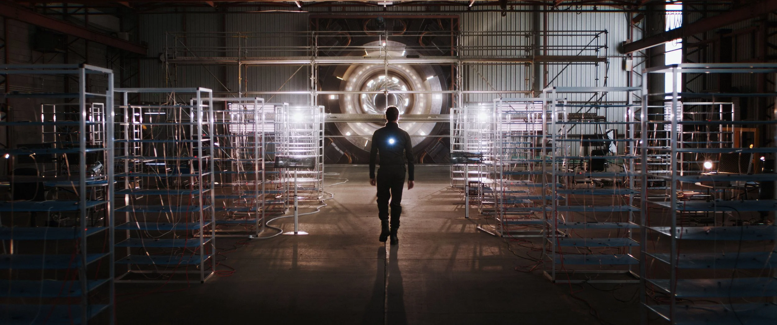 A person walking towards a large circular machine or tunnel inside an industrial or scientific facility, with metal scaffolding and equipment on either side.