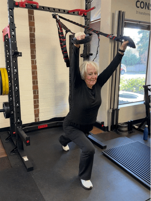 Elderly woman exercising with suspension straps in a gym.