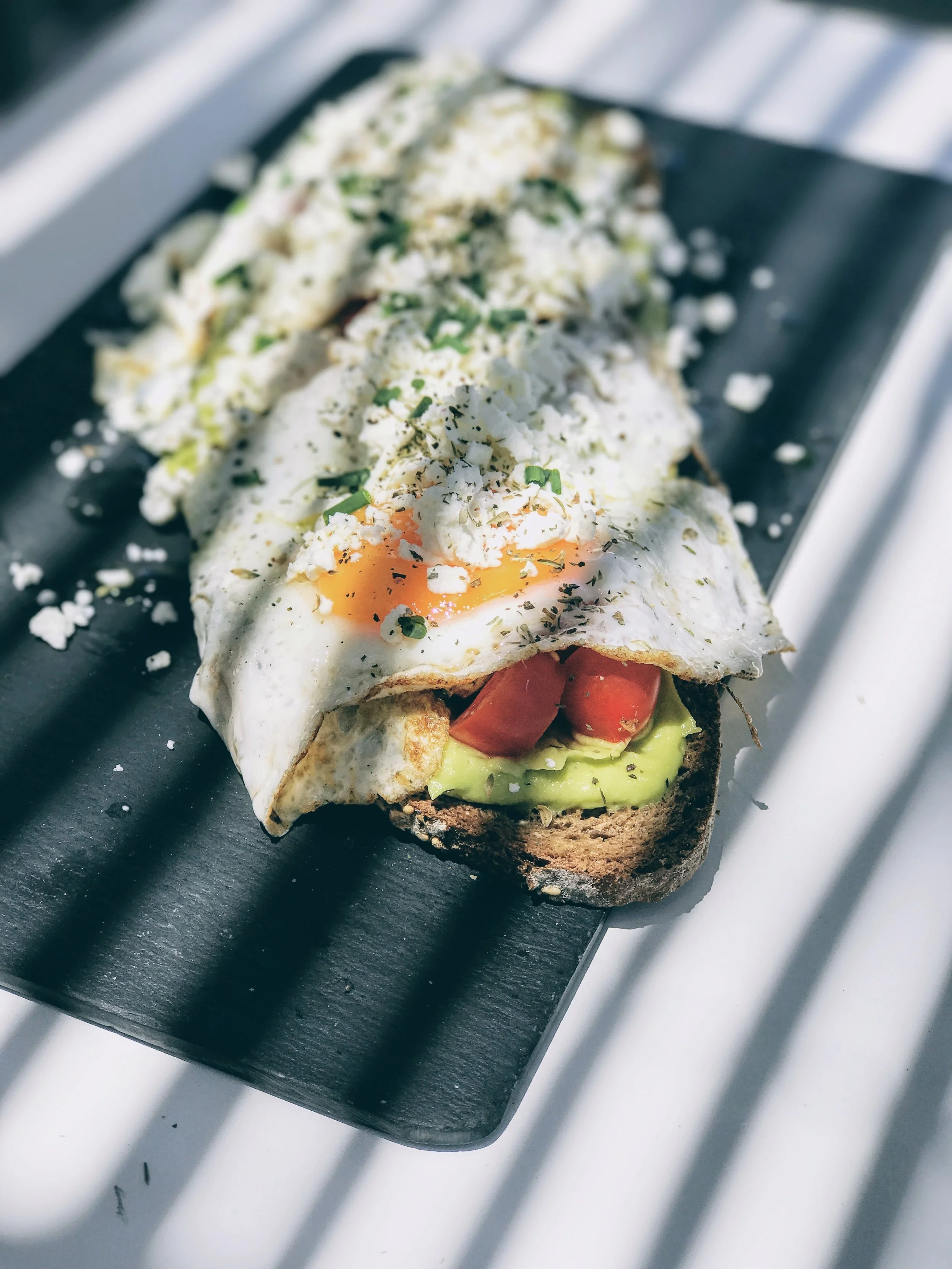 Easy sunny side up eggs on toasted brown bread, guacamole spread, pomodorini, feta cheese and fresh thyme