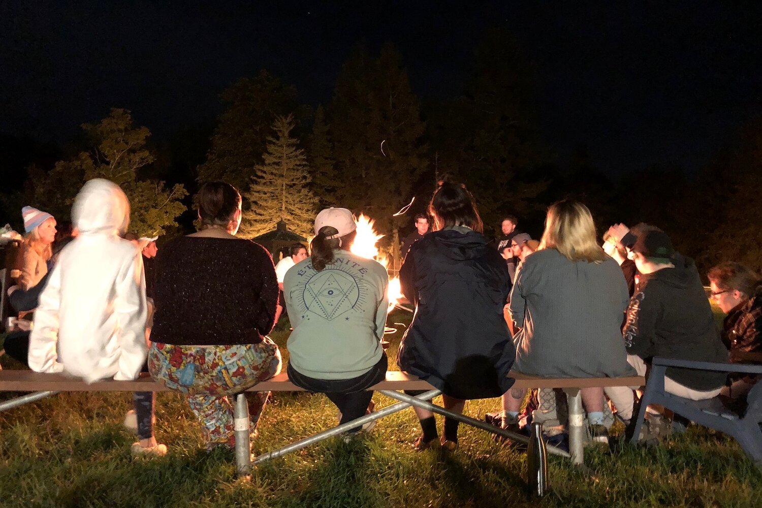  A line of teens sit in front of a campfire. 