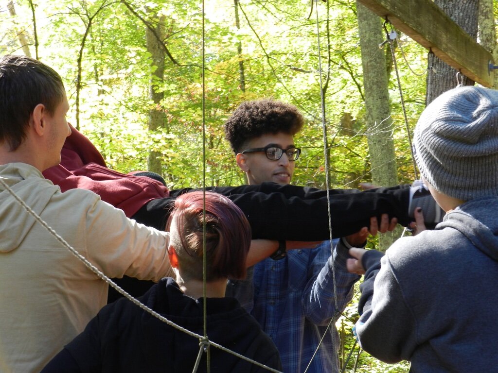  Attendees hold on to on another and ropes hanging from trees. 