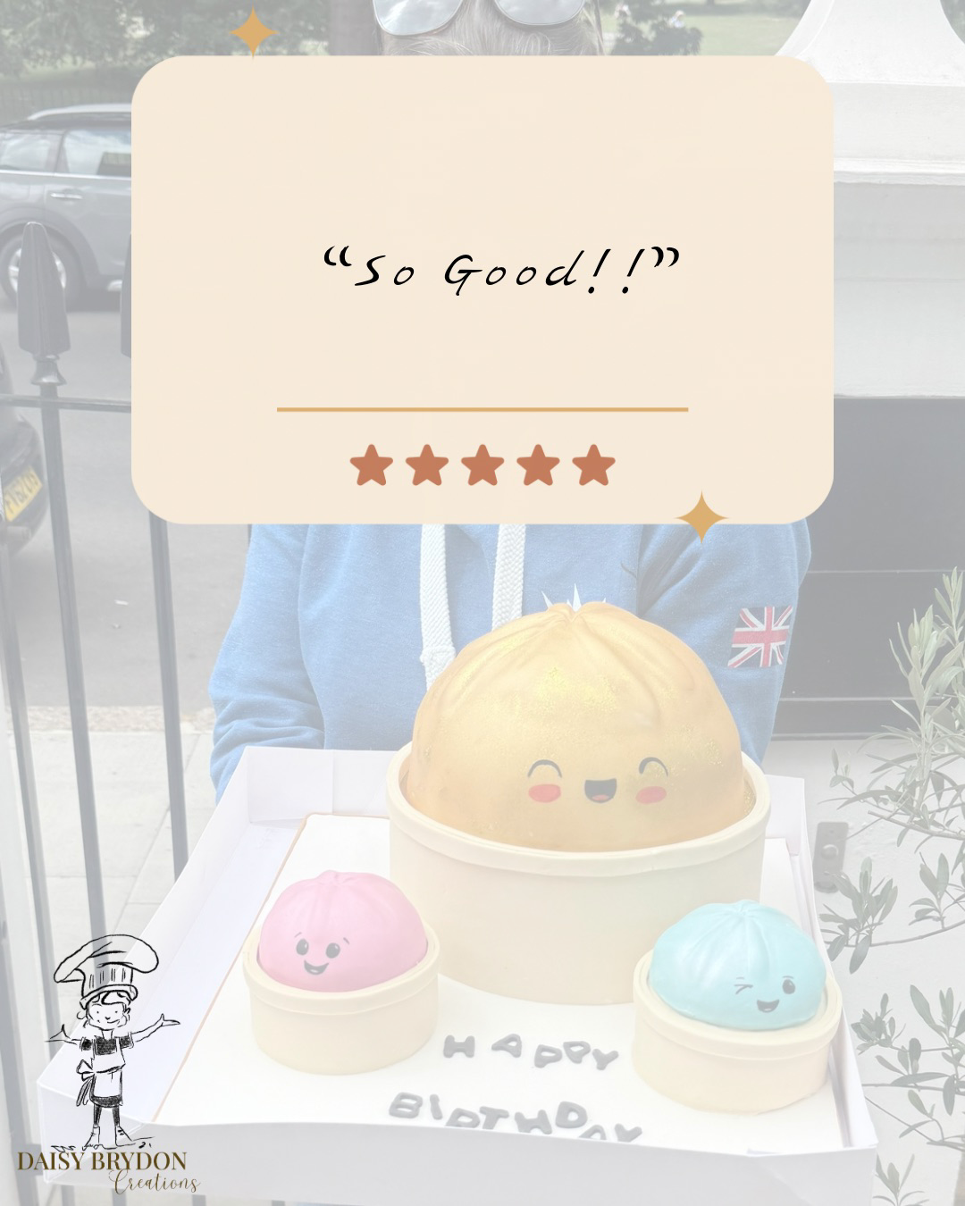 A birthday cake with three pastel-colored, cute, plush-like decorations on top, each with smiling faces, placed on a white tray. A beige sign overhead reads 'So Good!' with five stars below. The cake has the words 'HAPPY BIRTHDAY' written on it.
