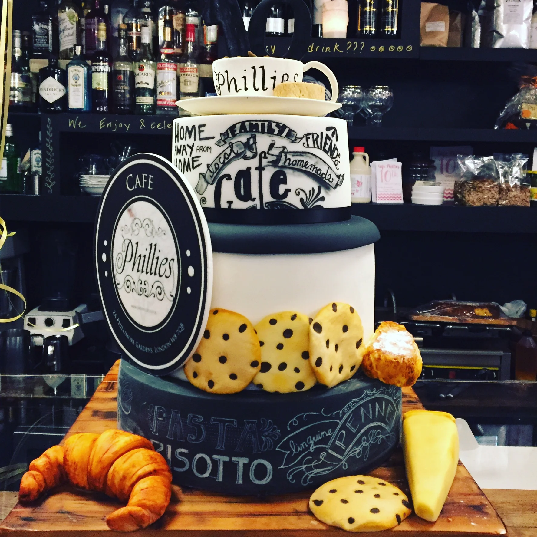 a 3 tier cake for Phillies cafe in Kensington, decorated with a chocolate croissant, cookies and florist paste cup and saucer