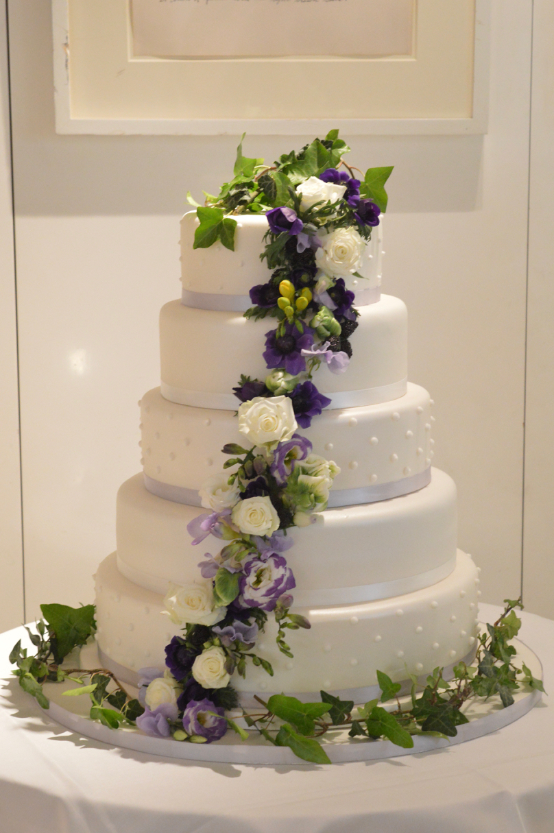 4 tier wedding cake with purple and cream fresh flowers down the centre