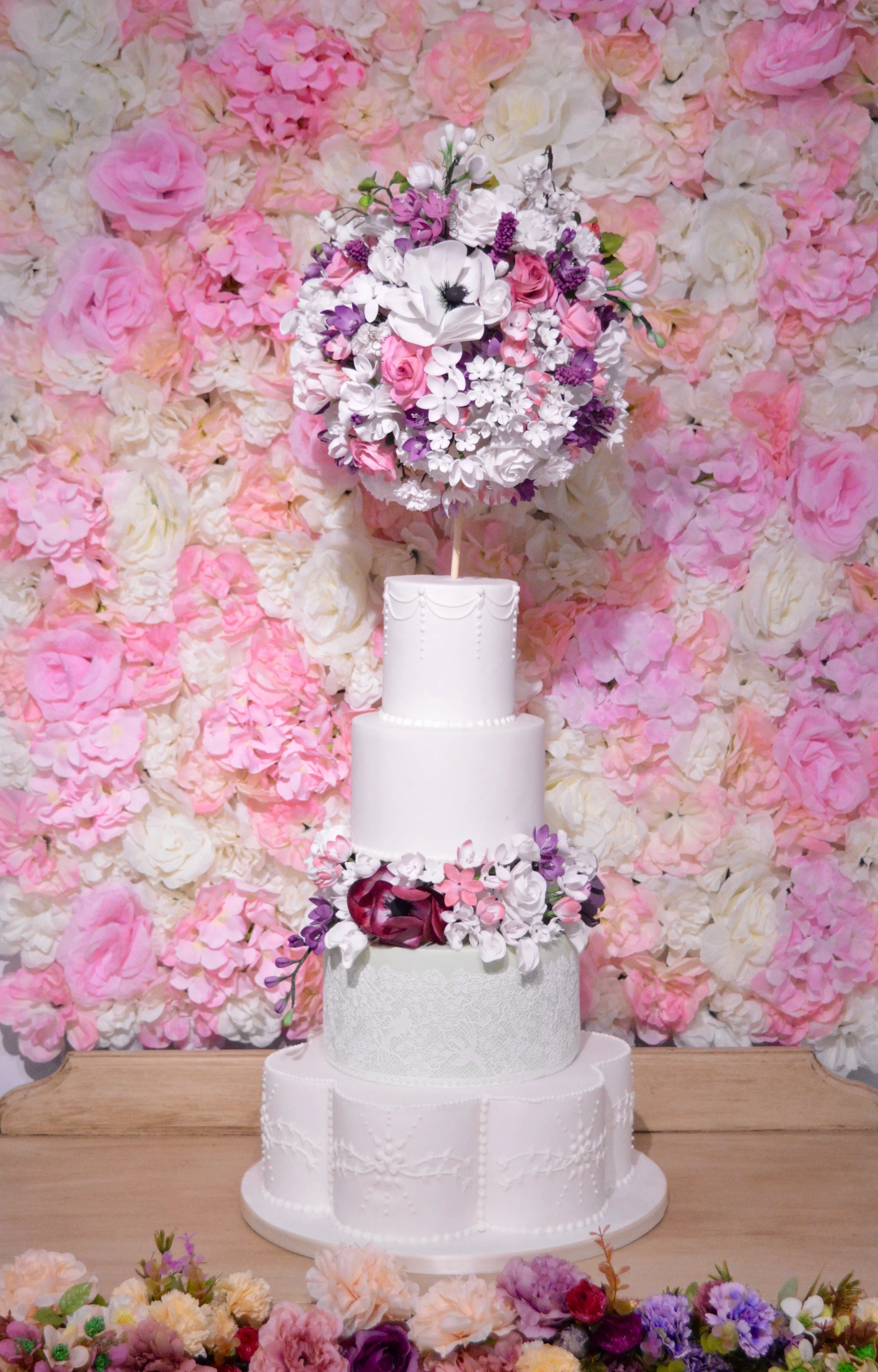 4 tier wedding cake. The bottom tier is a pettle shaped tier. The topper is a ball of sugarflowers